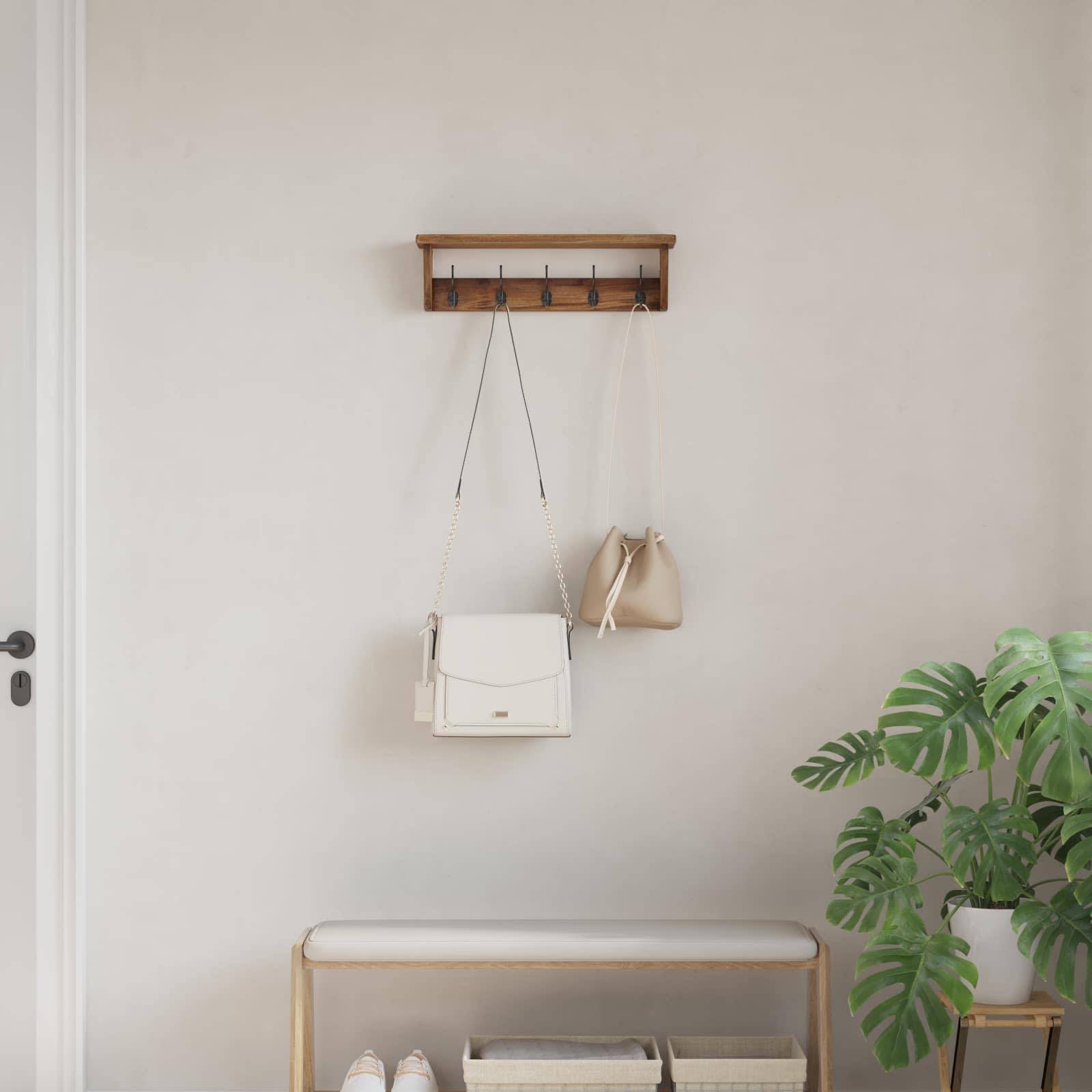 Eine kleine, minimalistische Diele mit einem Holzregal, das Handtaschen trägt, einer Bank darunter und einer Topfpflanze an der Seite.