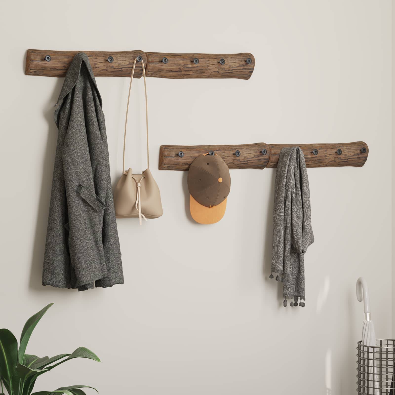 Eine rustikale Holz-Garderobe mit Haken trägt einen grauen Mantel, eine beige Tasche, eine orangefarbene Kappe und einen grauen Schal. Eine Topfpflanze ist unten links zu sehen.