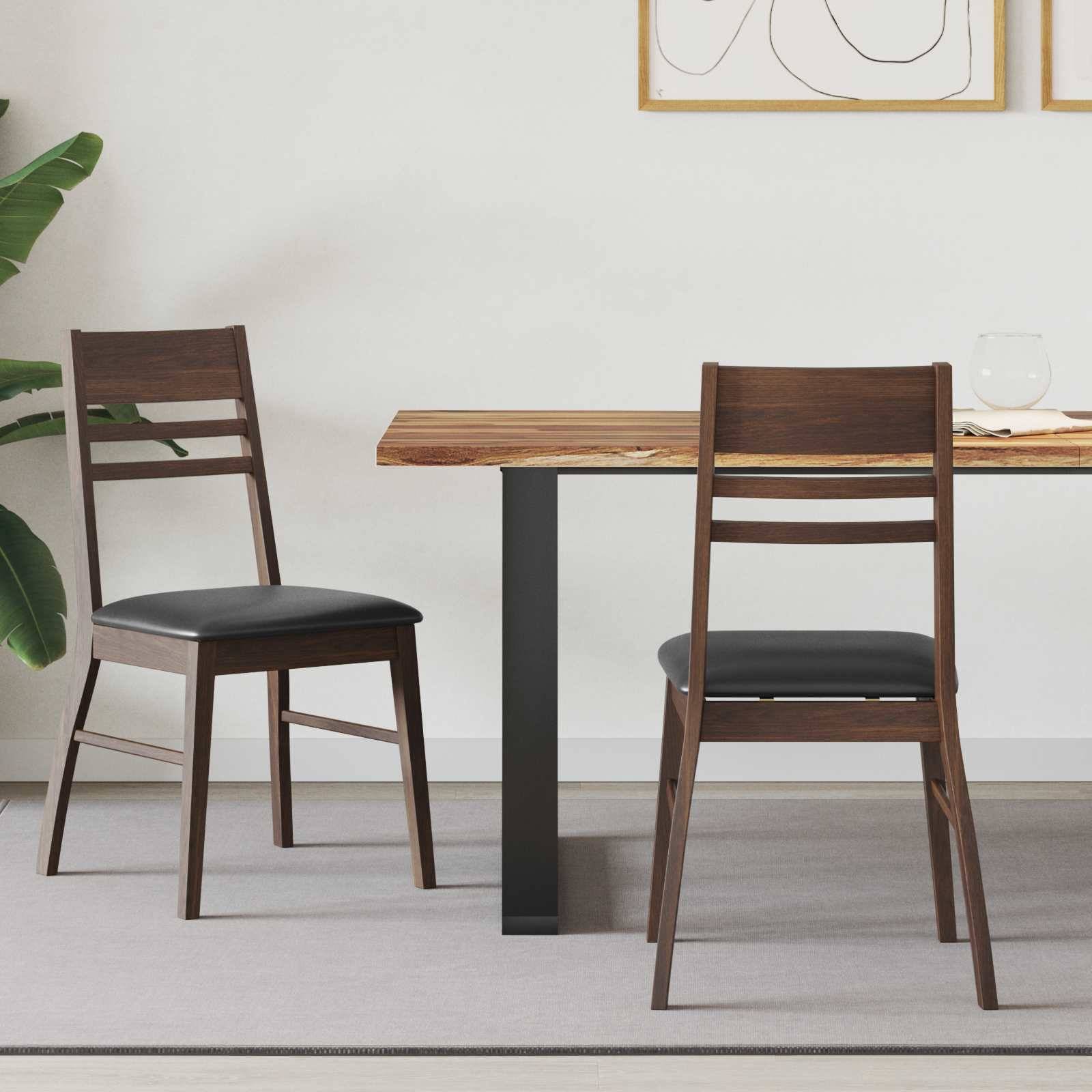 Ein minimalistischer Essbereich mit zwei Holzstühlen und einem rechteckigen Holztisch. Eine Blattpflanze steht in der Ecke, an der Wand hängt abstrakte Kunst.