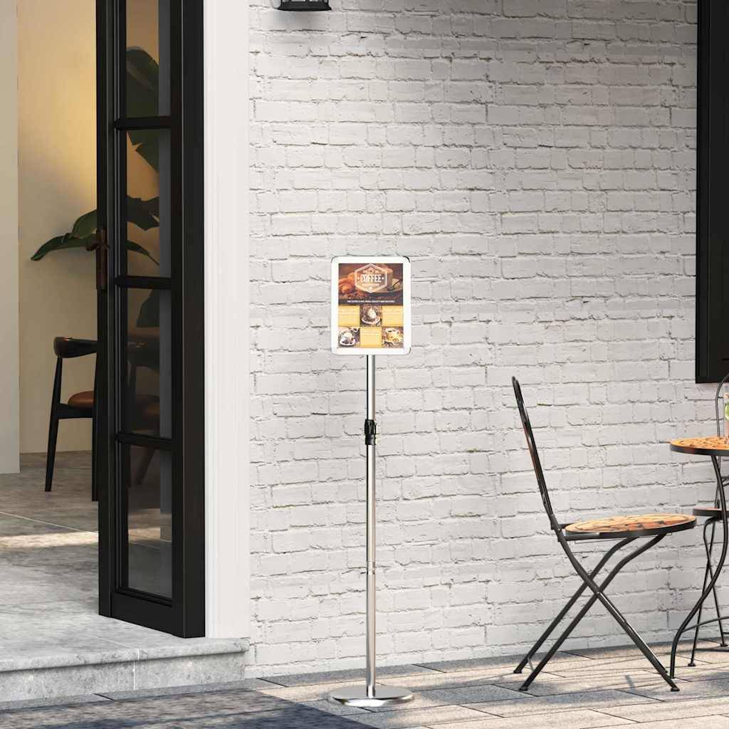 Ein Ständer mit einem gerahmten Menü vor dem Eingang eines Restaurants, neben einer schwarzgerahmten offenen Tür und einem zusammengeklappten Metallstuhl auf einer Steinterrasse.