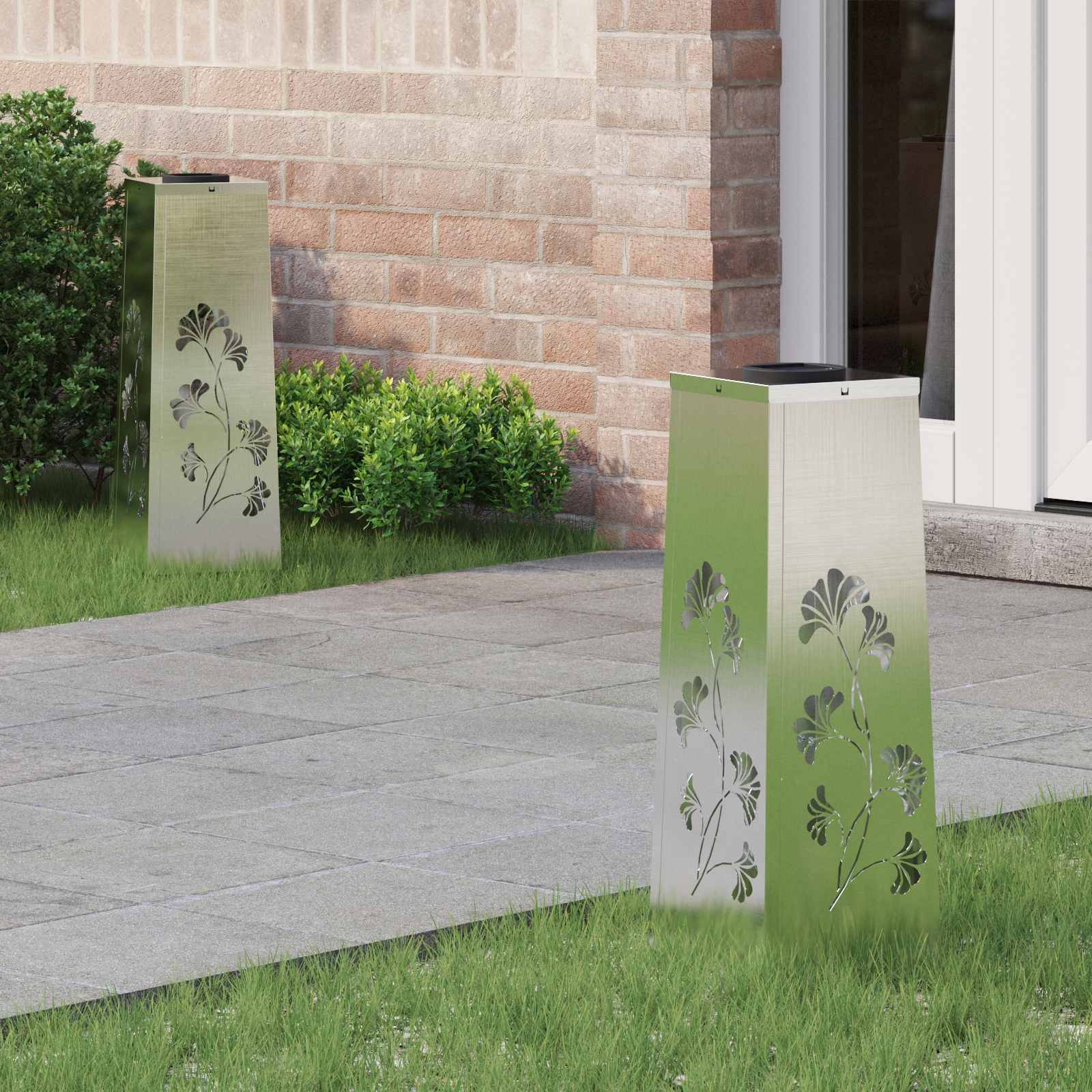 Zwei Metallsäulen mit Blumenausschnitten stehen auf einem gepflasterten Weg in der Nähe einer Backsteinmauer und Büschen und führen zum Eingang eines modernen Gebäudes.