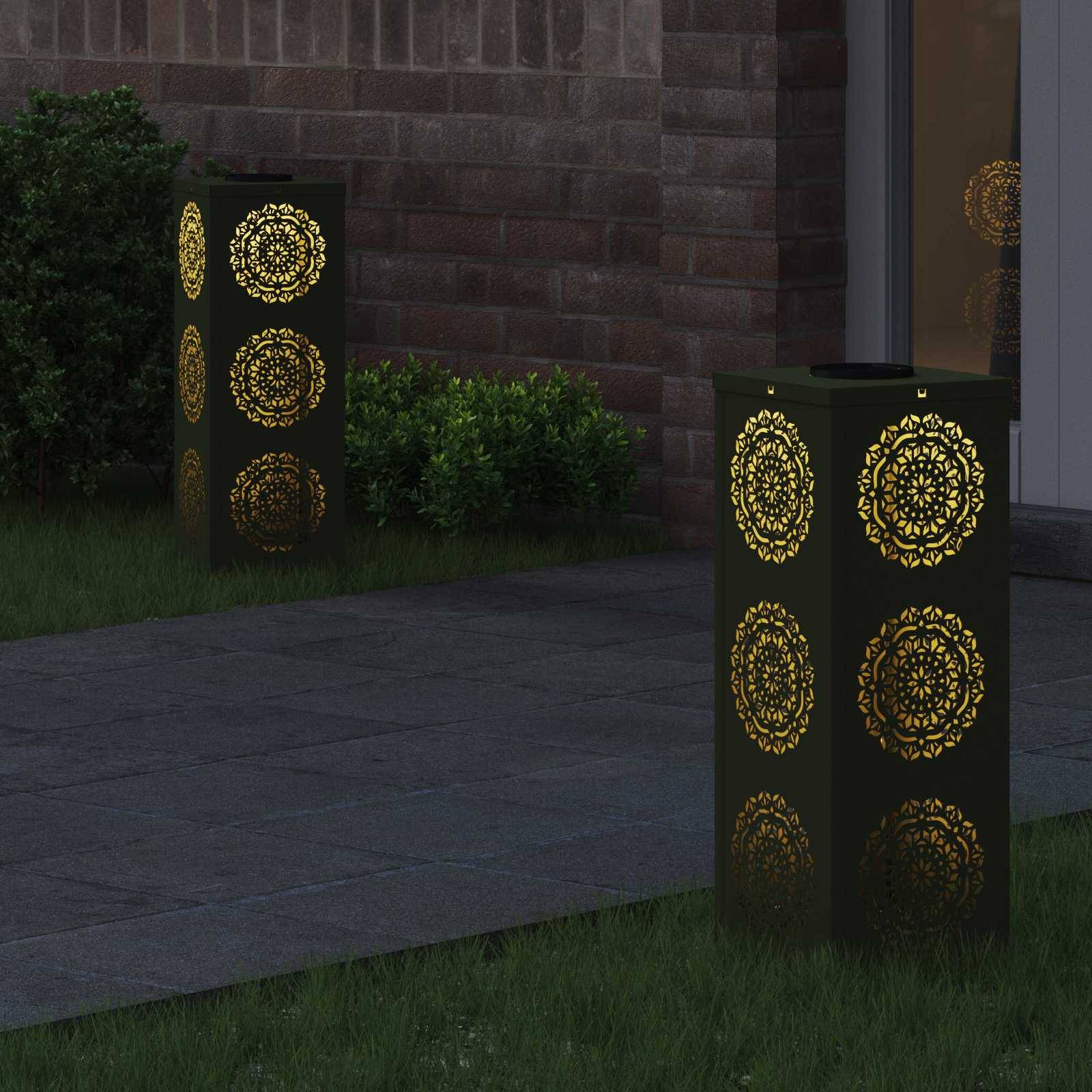 Zwei dekorative Außenlampen mit kunstvollen goldenen Mustern beleuchten einen Gartenpfad neben einem Gebäude in der Nacht.