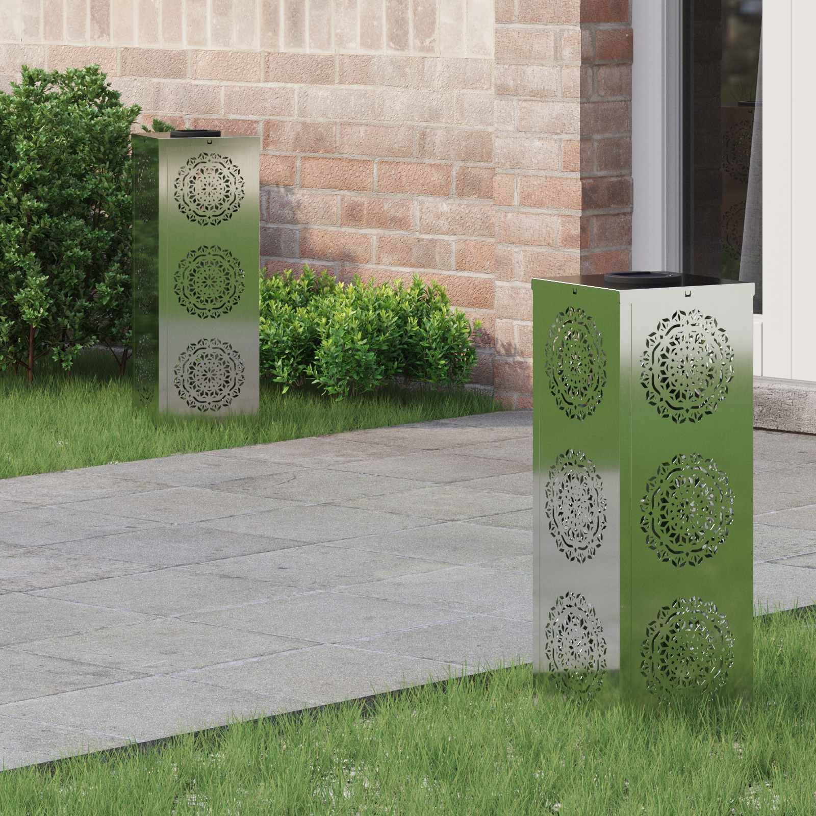 Zwei dekorative Metalllaternen mit kunstvollen Mustern stehen auf einem Gartenpfad in der Nähe von grünen Büschen und einer Ziegelwand.