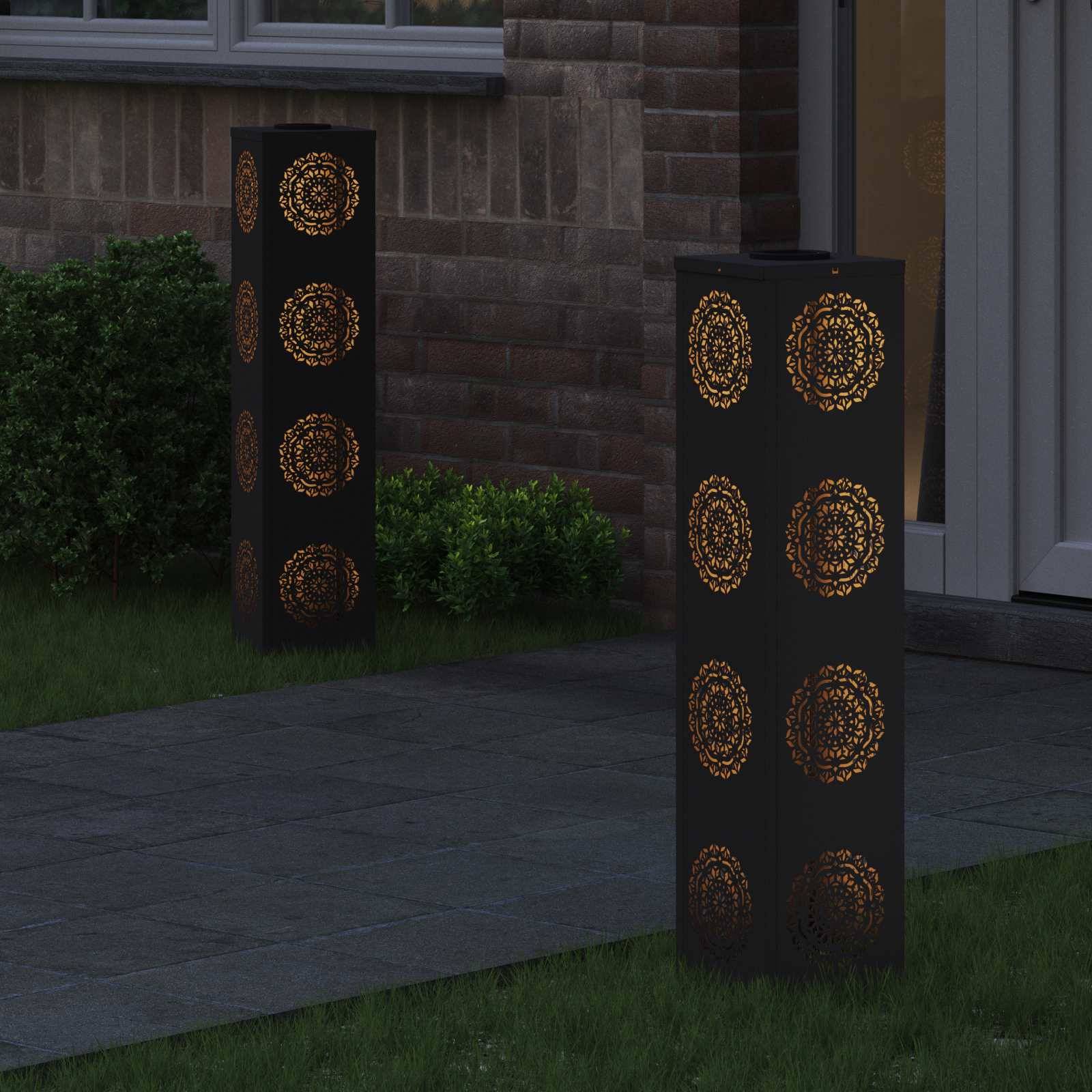 Außenlaterne mit verziertem Muster, beleuchtet in warmem Licht neben einer Ziegelwand und einem Garten, die die Abendstimmung verstärkt.