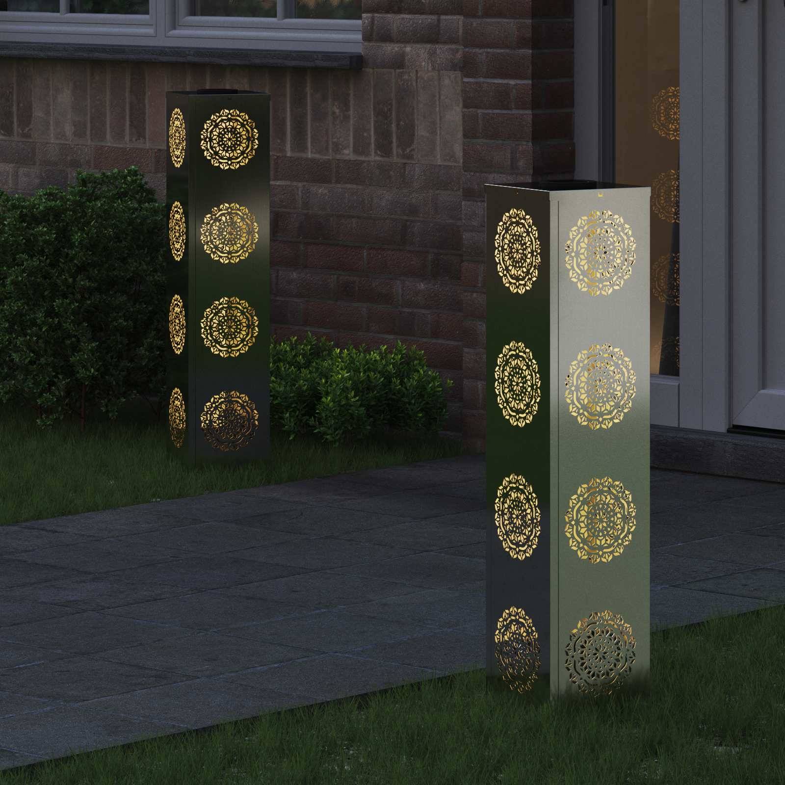 Beleuchtete Metalllaternen mit kunstvollen kreisförmigen Mustern beleuchten einen Weg entlang einer Ziegelwand und verleihen der Umgebung eine dekorative und warme Atmosphäre.