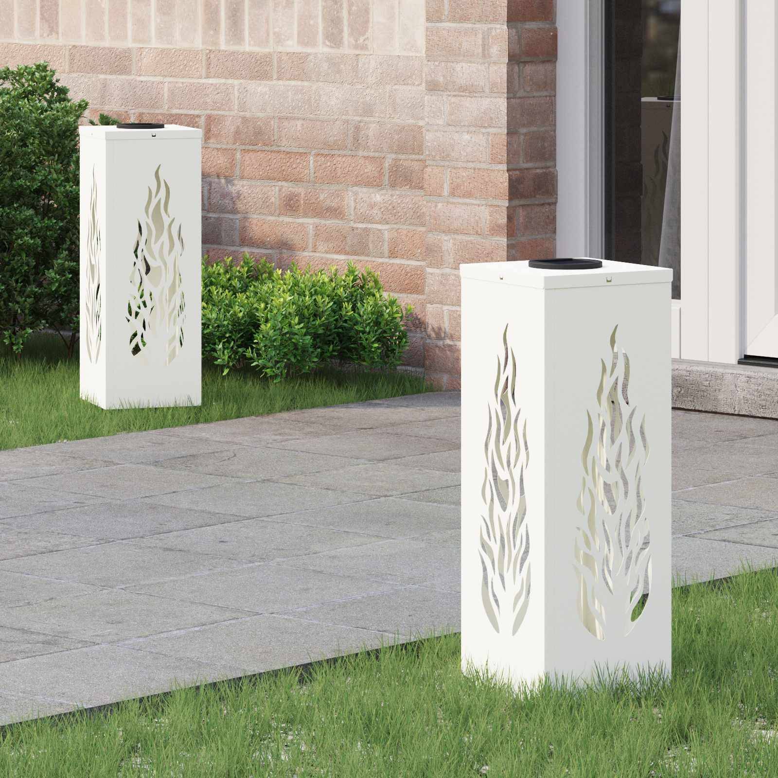 Zwei weiße, dekorative Außenlampen mit Flammenschnittmustern stehen auf einem gepflasterten Weg neben einer Ziegelwand und kleinen grünen Sträuchern.