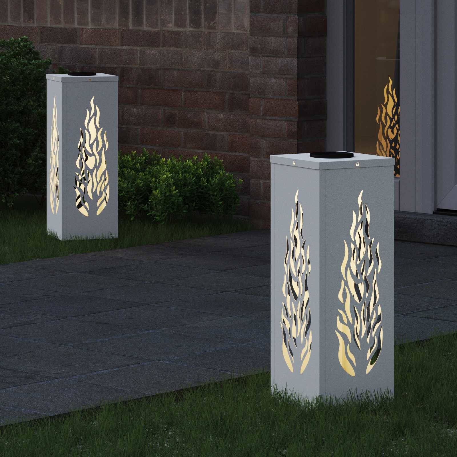 Außenlaternen mit ausgeschnittenen Flammendesigns beleuchten einen Weg in der Nacht neben einem Gebäude und Gartensträuchern.