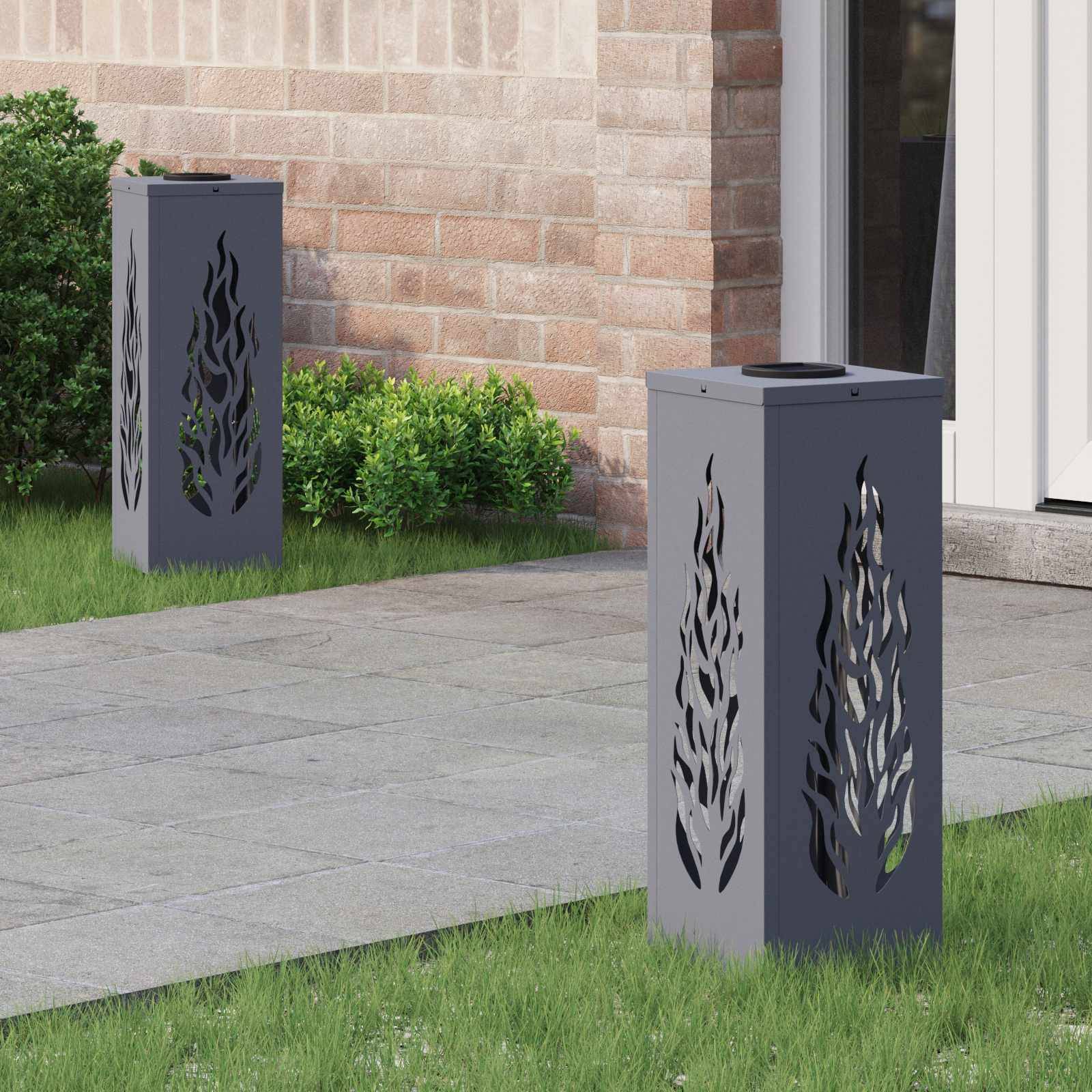 Moderner Garten mit zwei dekorativen Metalllaternen mit Flammenschnittmustern, die auf einer Steinterrasse in der Nähe des Hauseingangs und grüner Büsche platziert sind.