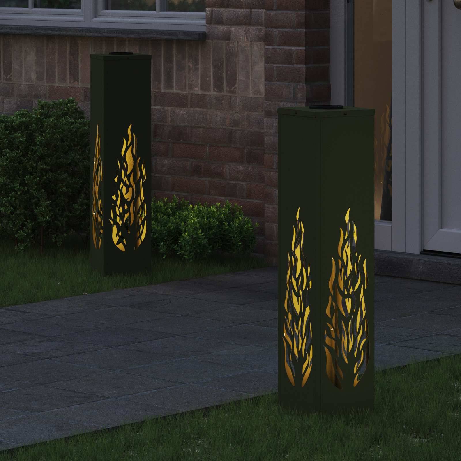 Zwei dekorative Laternen mit flammenartigen Ausschnitten sind entlang eines Gartenpfads nahe einer Ziegelwand platziert und sorgen für stimmungsvolle Beleuchtung.