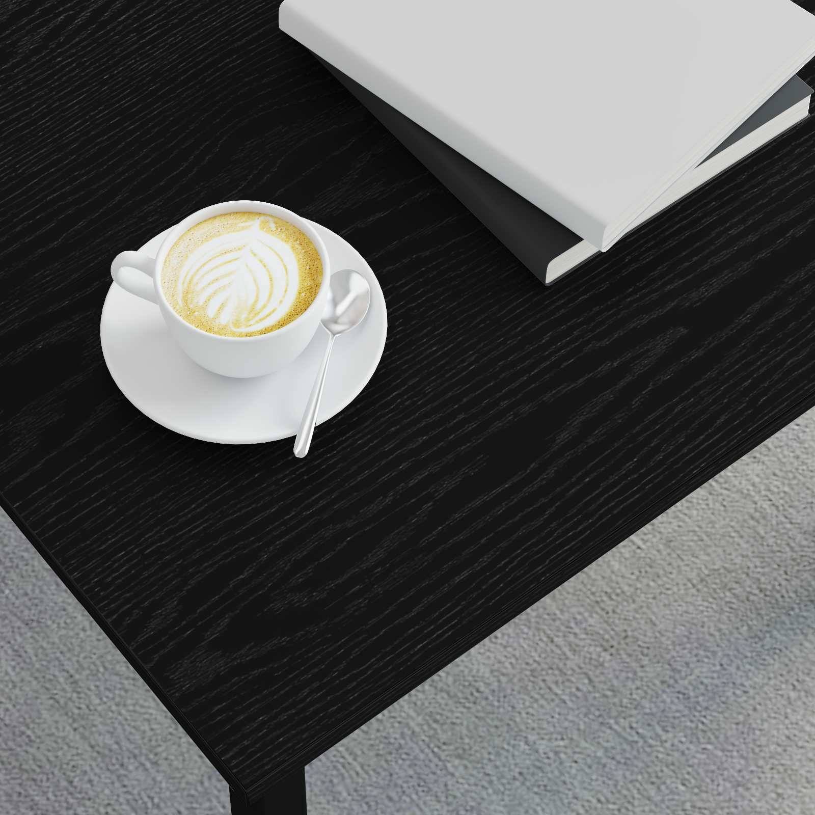 Eine Tasse Latte mit Latte-Art-Design und einem Löffel auf einer Untertasse, die auf einem schwarzen Holztisch neben einem geschlossenen weißen Buch steht.