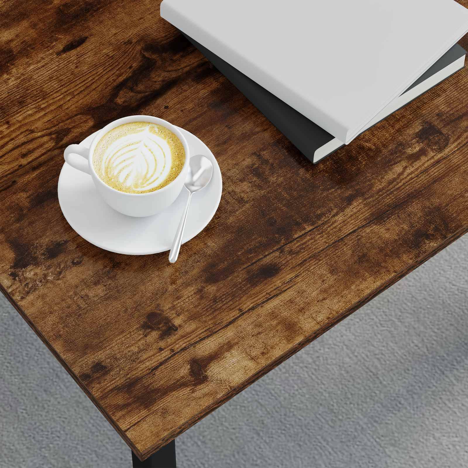 Eine Tasse Kaffee mit Latte Art und einem Löffelablage ruhen auf einem Unterteller auf einem Holztisch. Ein geschlossenes Buch liegt neben der Tasse.