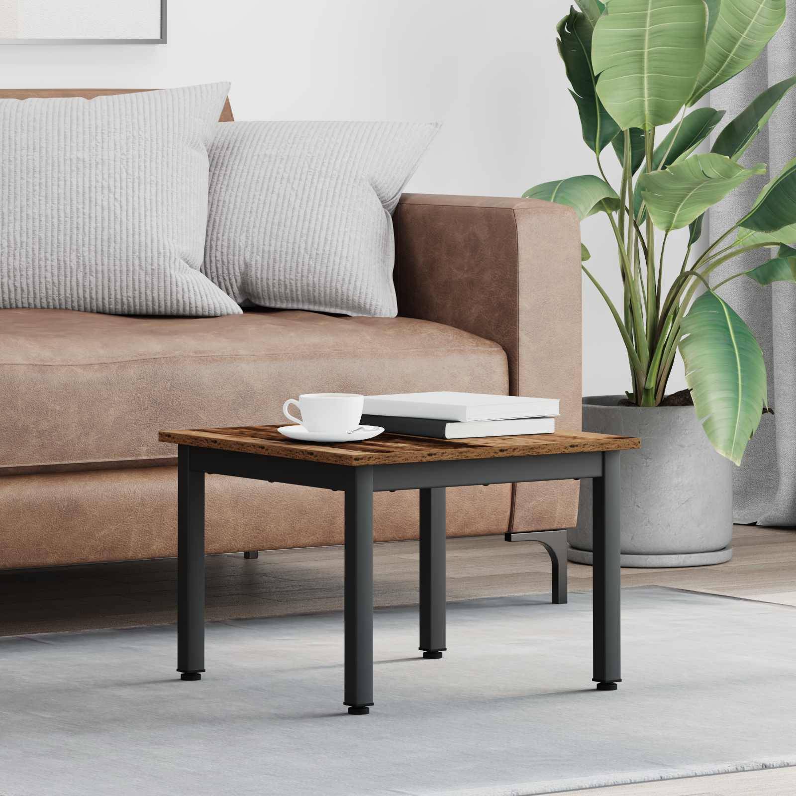 Ein gemütliches Wohnzimmer mit einem braunen Sofa, zwei gestreiften Kissen, einem kleinen Couchtisch und einer großen blattreichen Pflanze in der Ecke.