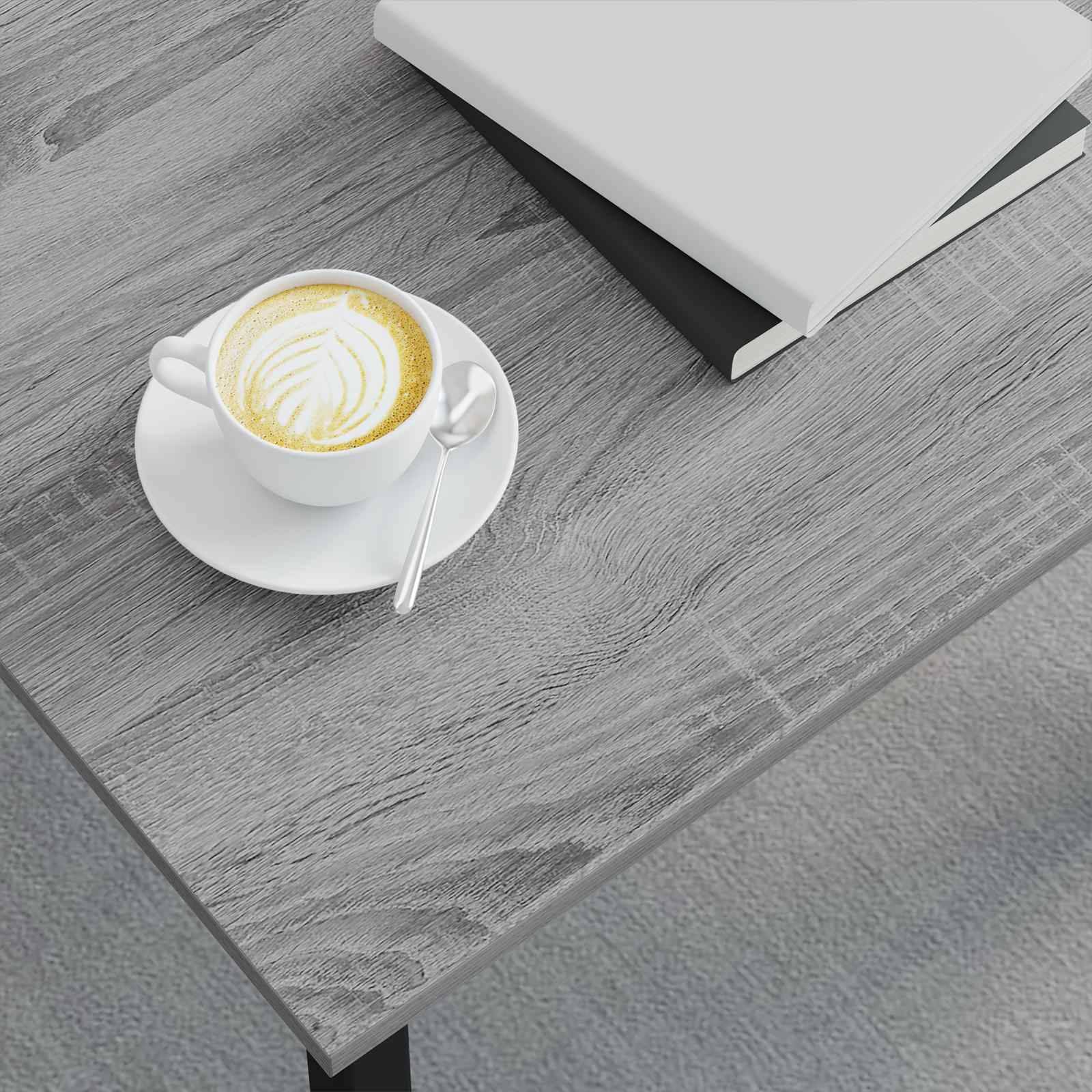 Eine Latte mit Schaum-Kunst in einer weißen Tasse auf einem Unterteller steht neben einem geschlossenen Buch auf einem Holztisch.