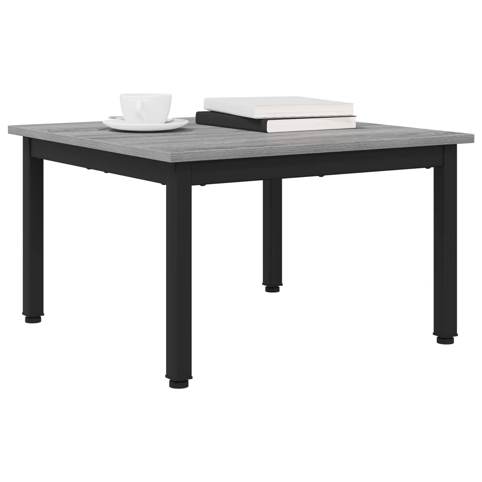 Ein quadratischer, grauer Couchtisch mit schwarzen Metallbeinen, auf dem eine weiße Tasse und Untertasse sowie zwei geschlossene Bücher platziert sind.