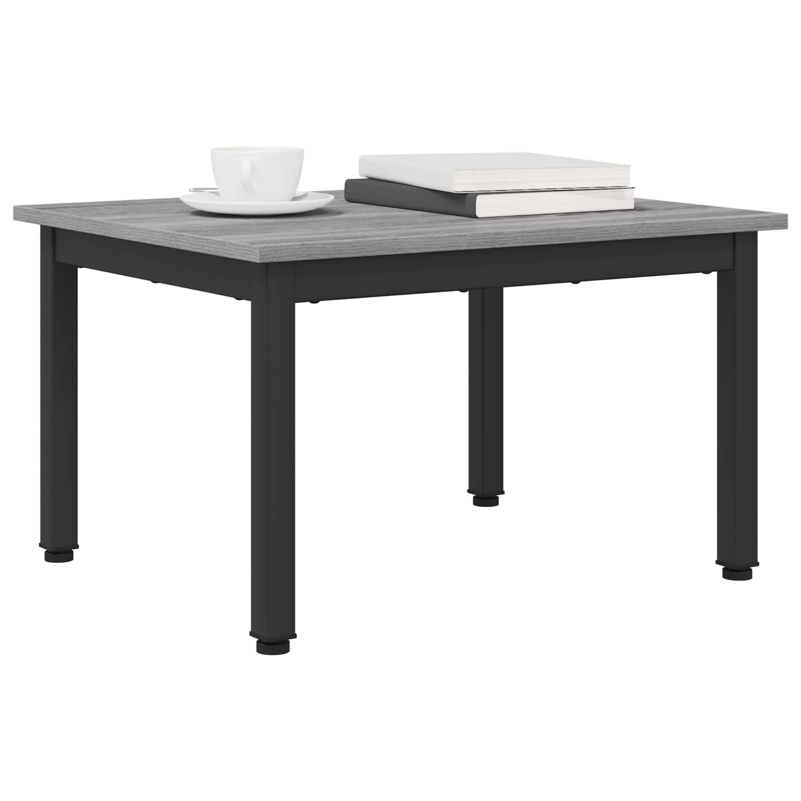 Ein quadratischer, grauer Tisch mit schwarzen Beinen, auf dem eine weiße Tasse mit Untertasse und zwei geschlossene Bücher, die rechts aufgestapelt sind, stehen.