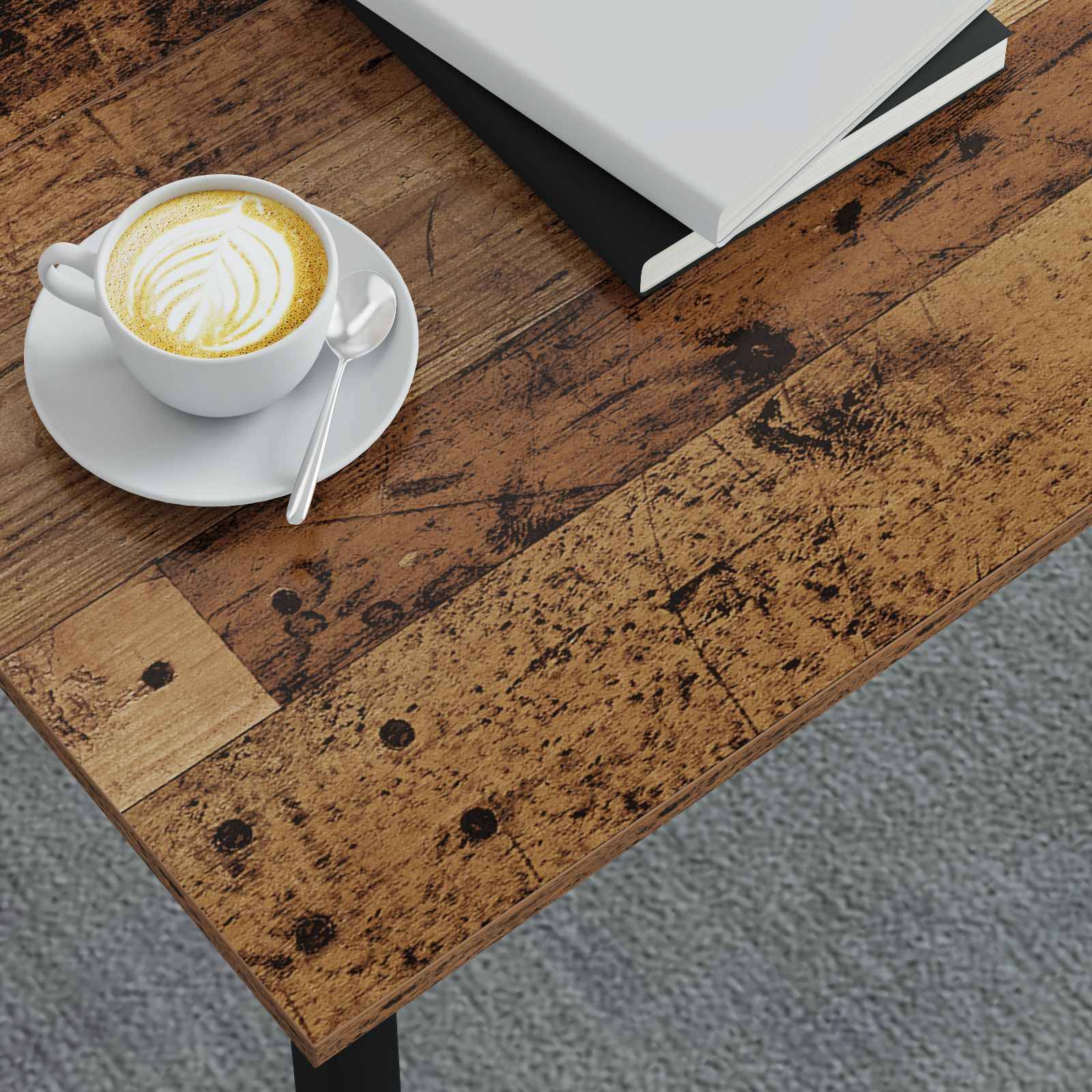 Ein Cappuccino mit Latte Art steht auf einer Untertasse mit einem Löffel, neben geschlossenen Büchern auf einem Holztisch mit strukturierter Oberfläche.