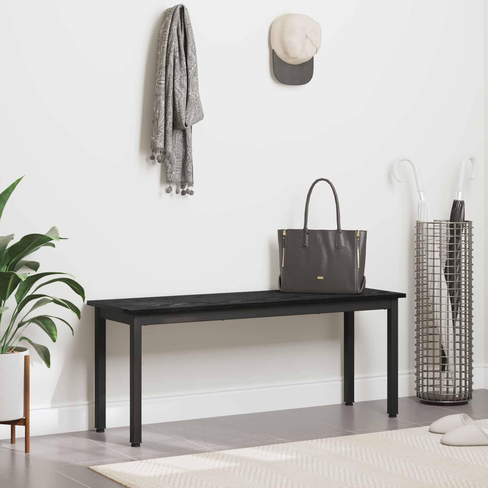 Ein moderner Eingangsbereich zeigt eine schwarze Bank, eine hängende graue Tasche und Mütze sowie einen nahegelegenen Pflanzen- und Schirmständer, wodurch eine minimalistische Dekoration entsteht.
