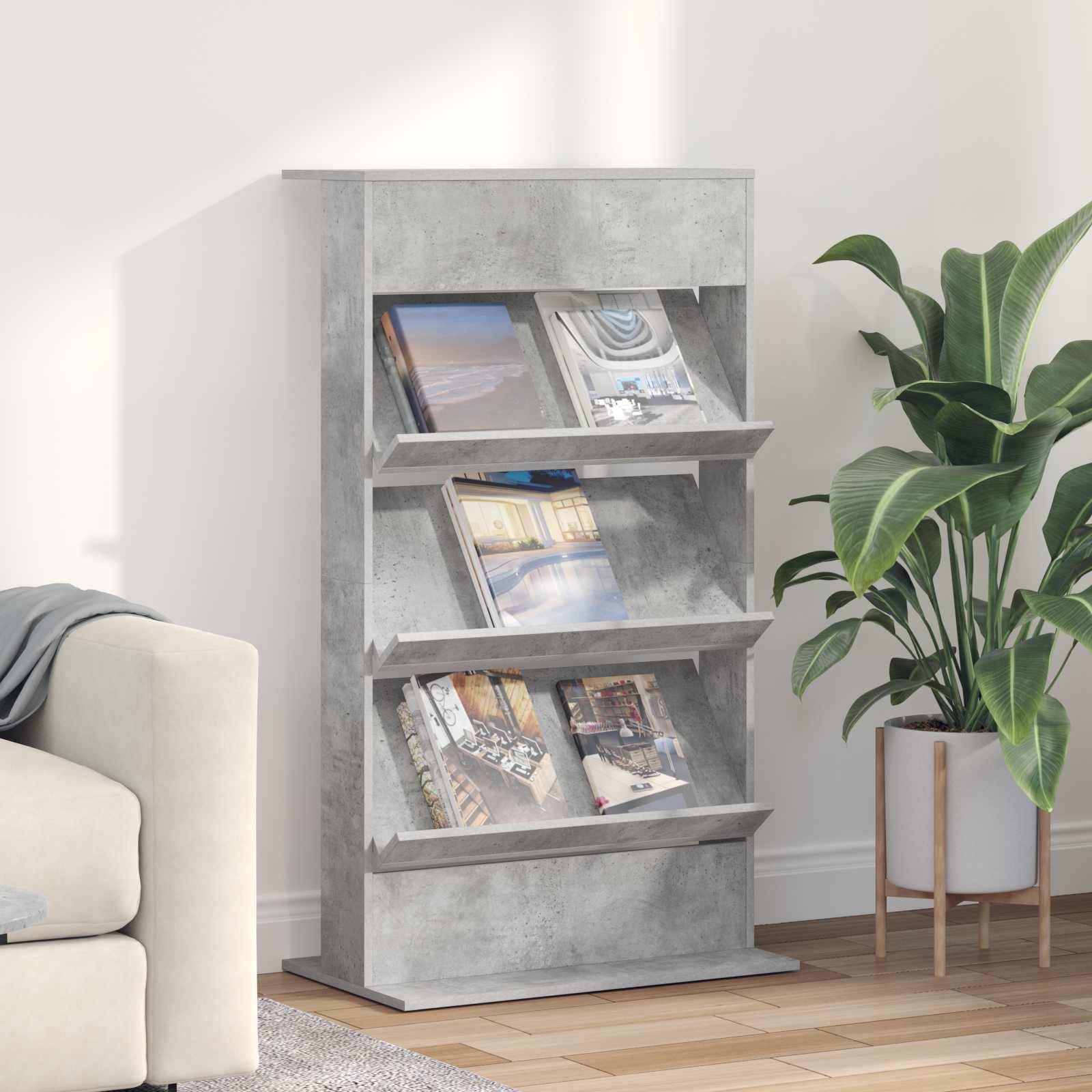 Ein modernes, graues Bücherregal steht in einem Wohnzimmer und präsentiert Zeitschriften. Es befindet sich neben einer Topfpflanze, in der Nähe eines hellgefärbten Sofas.
