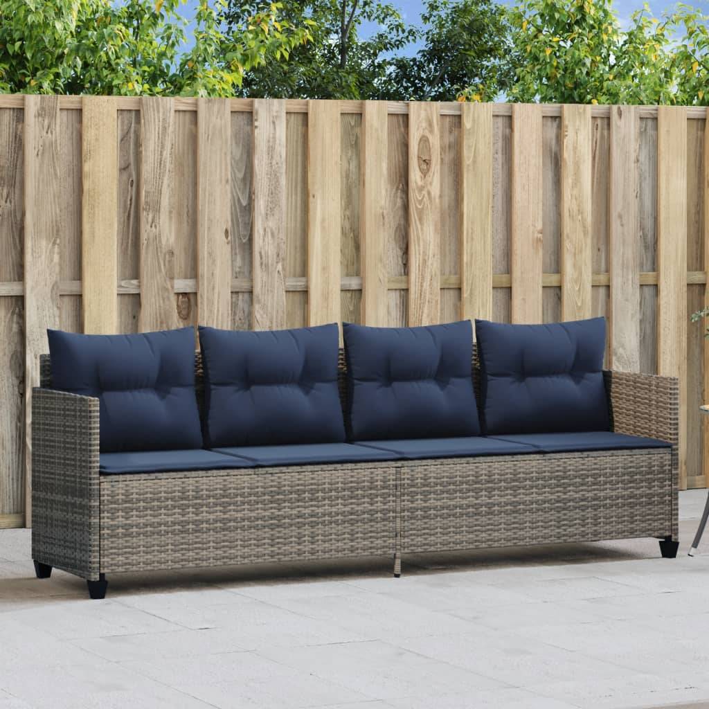 Outdoor-Rattansofa mit Marineblau-Kissen, das vor einem Holzzaun steht, platziert auf einer Terrasse mit Bäumen im Hintergrund.