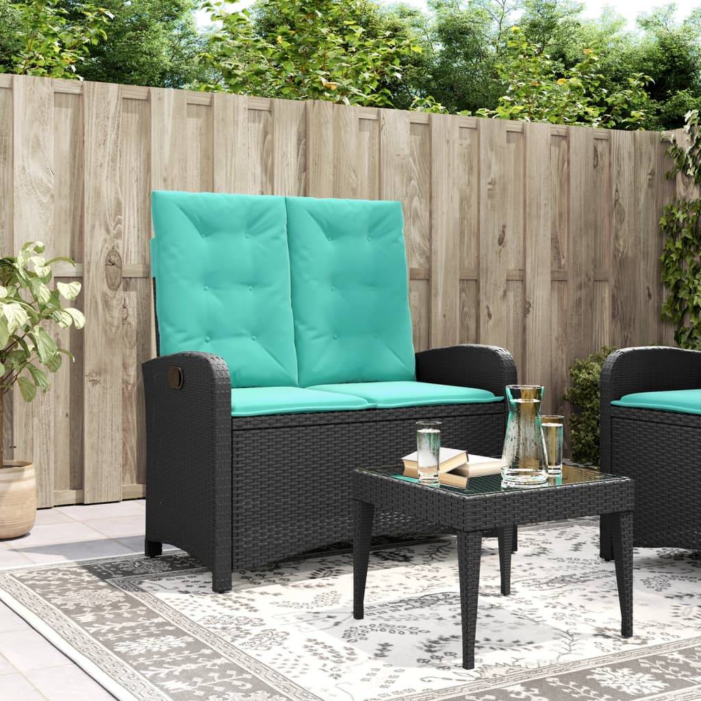 Gartenmöbel-Set mit schwarzen Rattanstühlen, petrolblauen Kissen, Glastisch; Topfpflanze in der Nähe, Holzzaun im Hintergrund. Gemütliche Außeneinrichtung.