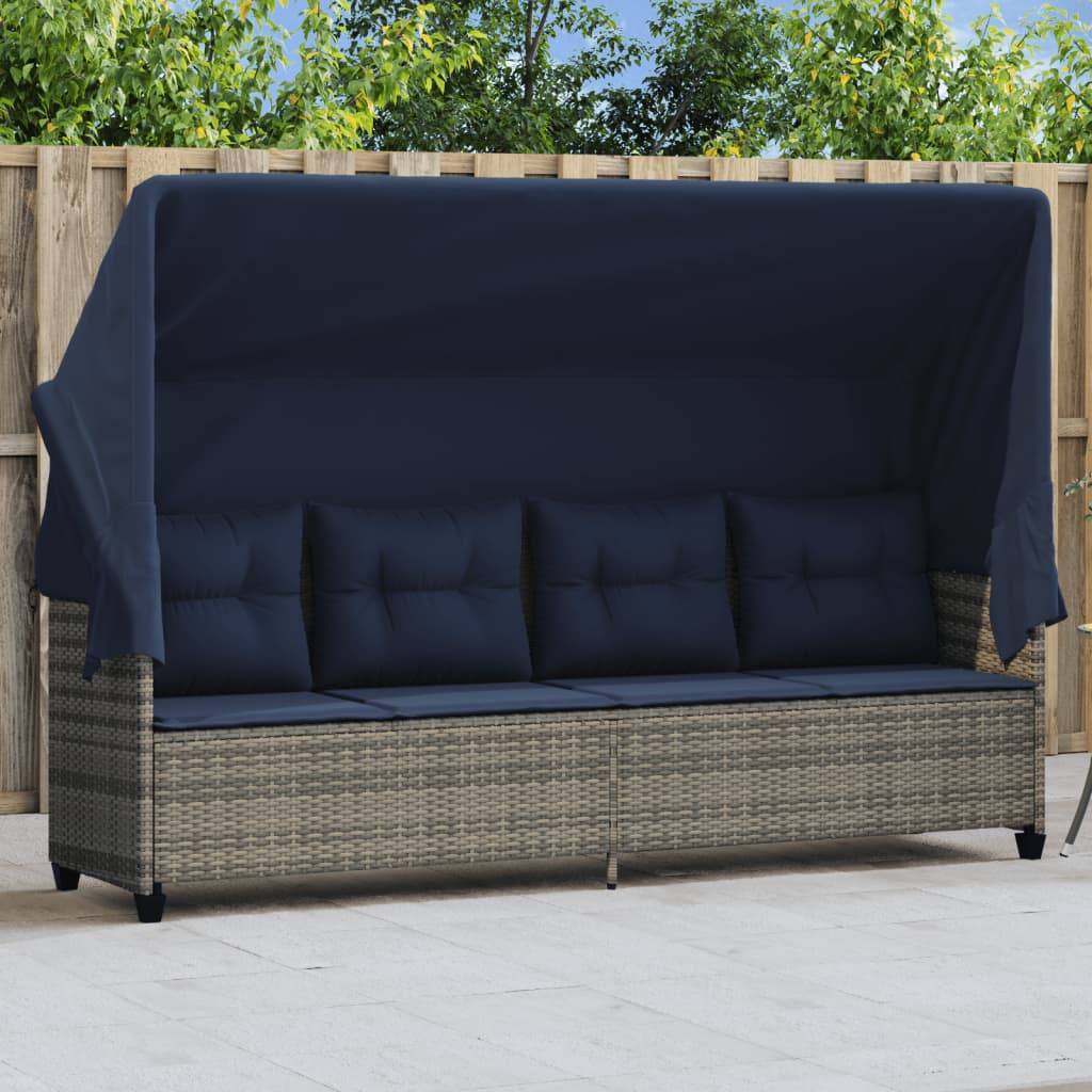 Outdoor-Rattansofa mit einem blauen Baldachin und Kissen, vor einem Holzzaun platziert und von Grünpflanzen in einer Terrassenumgebung umgeben.