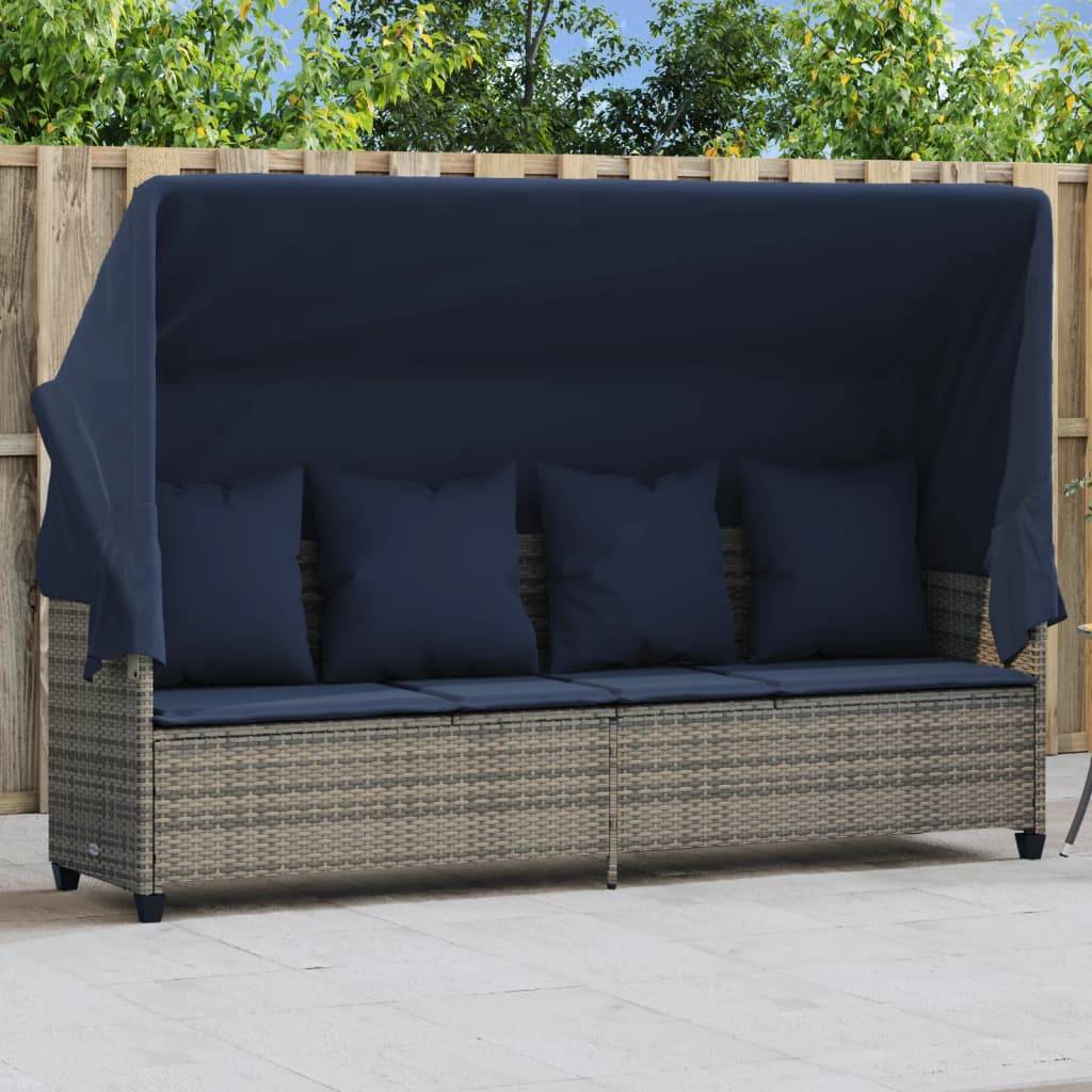 Dreisitziges Outdoor-Rattansofa mit dunkelblauen Kissen und einem Baldachin, aufgestellt auf einer Terrasse mit einer Holzzaunkulisse und Grünpflanzen im Hintergrund.