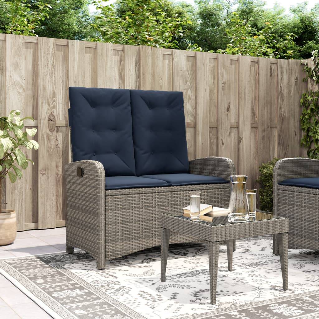 Outdoor-Terrasse mit einem Korbgeflecht-Zweisitzer, blauen Kissen und einem kleinen Glastisch. Umgeben von Pflanzen und einem Holzzaun. Friedliche Atmosphäre.