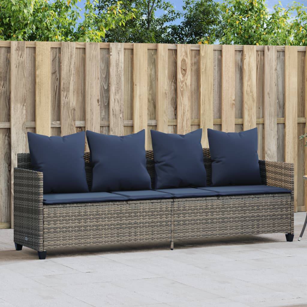 Outdoor-Rattansofa mit blauen Kissen auf einer Terrasse, im Hintergrund ein Holzzaun und umgeben von Grünpflanzen.