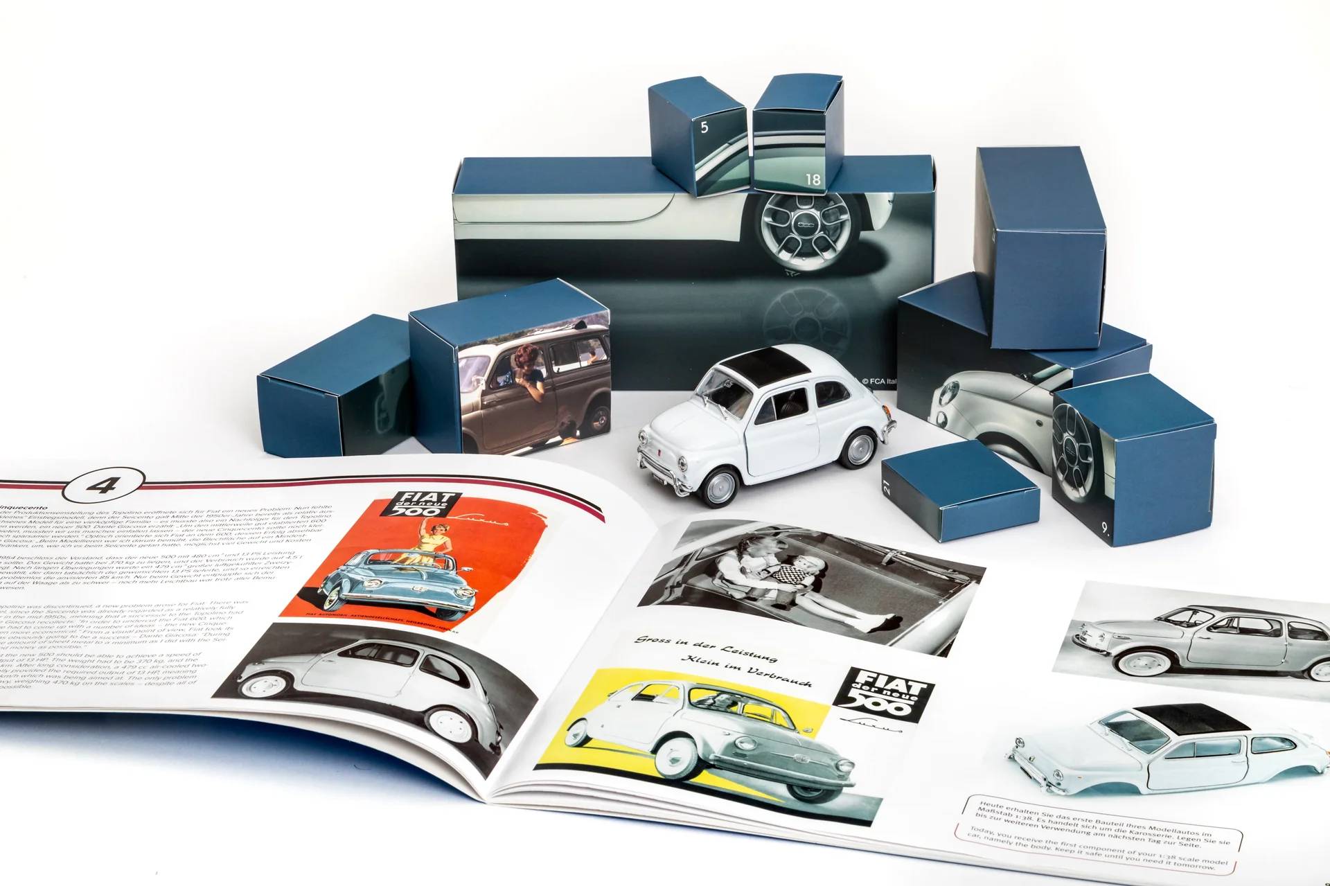 Ein klassisches Fiat 500 Modellauto, umgeben von Werbeprospekten und blauen Geschenkkartons, das das Design des Autos und historische Werbeanzeigen präsentiert.