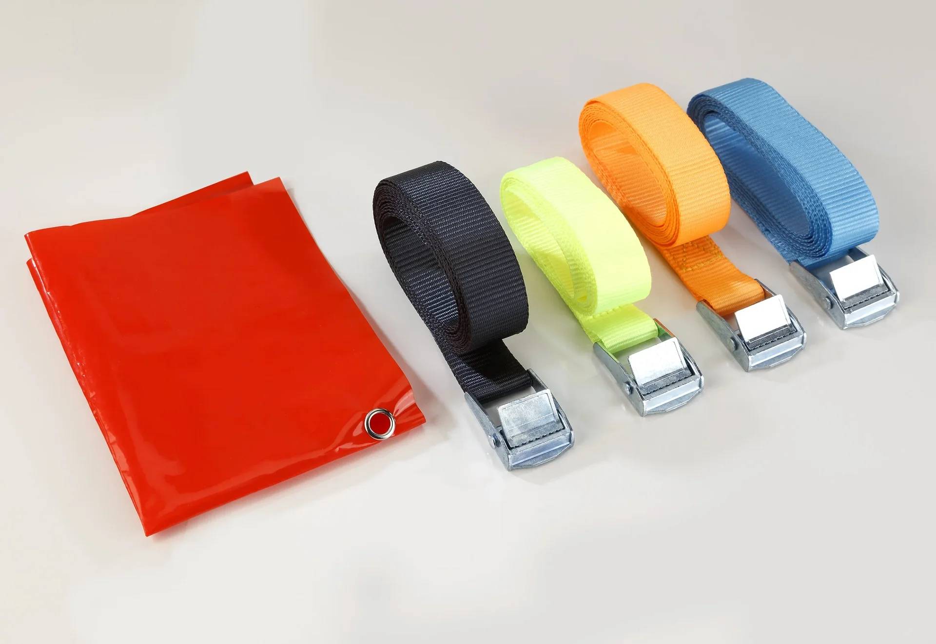 Eine rote Plane mit einer Metalltülle, die neben vier zusammengerollten Riemen in Schwarz, Gelb, Orange und Blau liegt, wobei jeder Riemen mit einer Metallschnalle versehen ist.