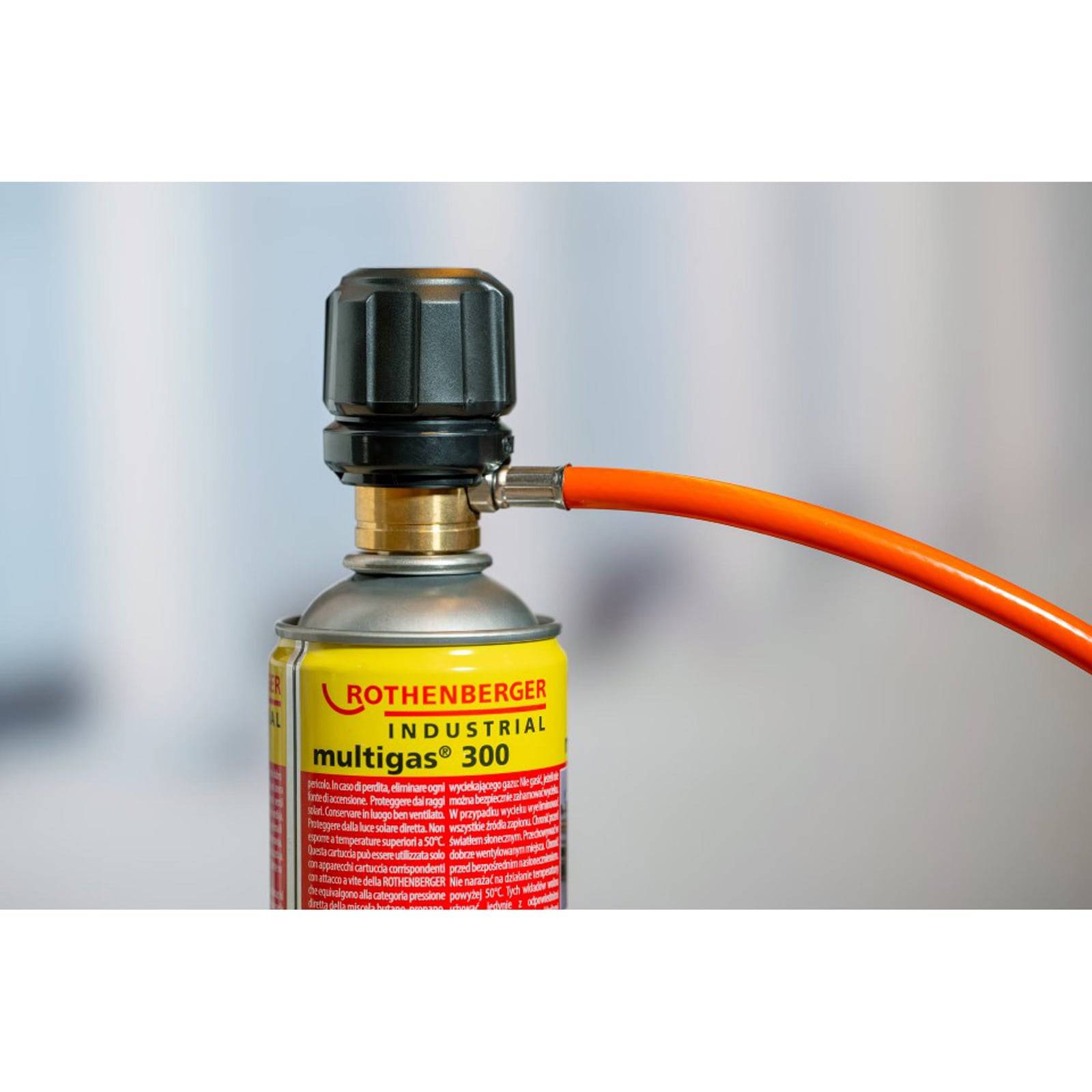 Eine Nahaufnahme einer Rothenberger Multigas 300 Kartusche mit schwarzem Deckel und angeschlossenem orangefarbenen Schlauch, die für industrielle Zwecke verwendet wird.