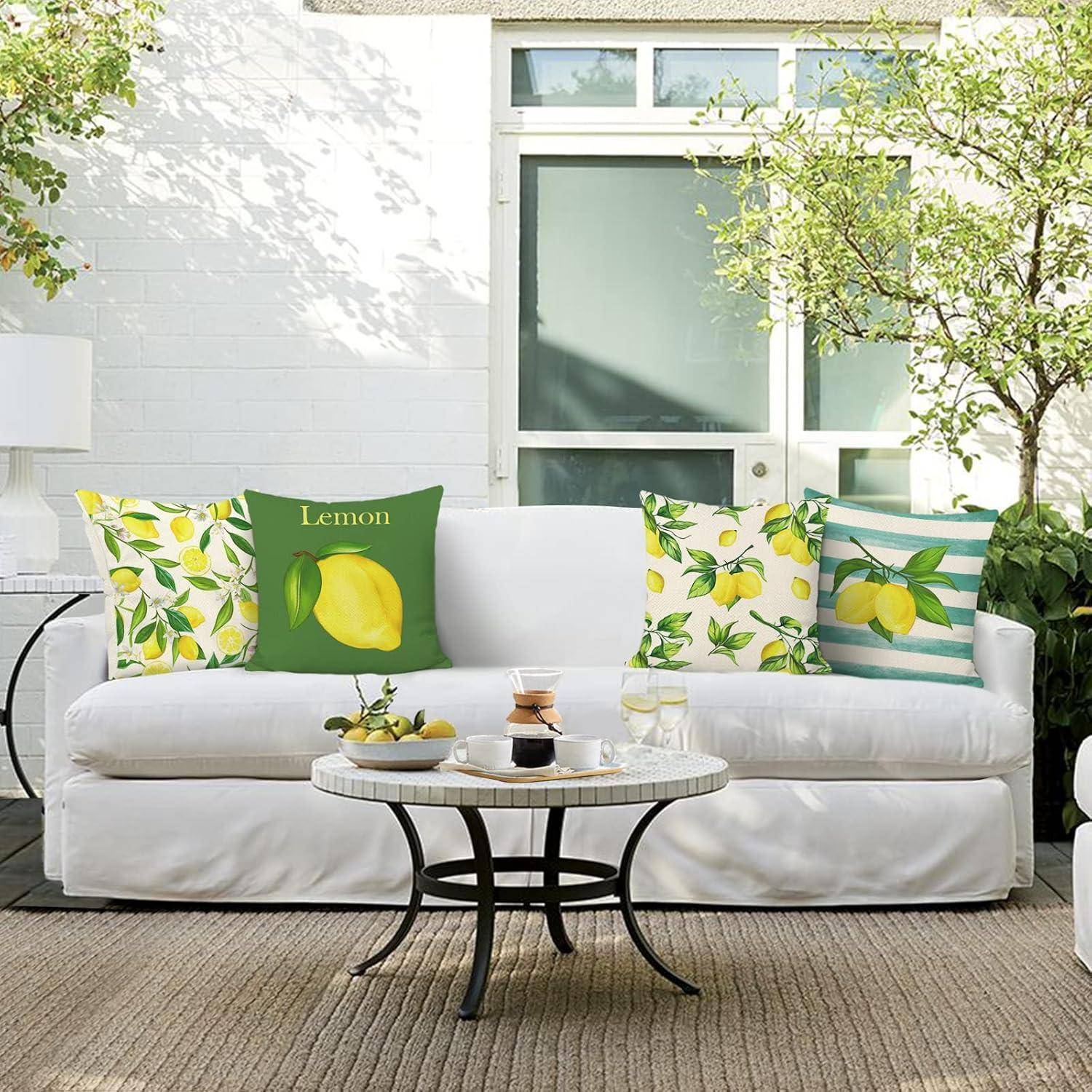 Eine weiße Outdoor-Couch mit zitronen-thematischen Kissen ist an einer Patiowand platziert, nahe einem kleinen Tisch und einem sonnenbeschienenen Zitronenbaum.