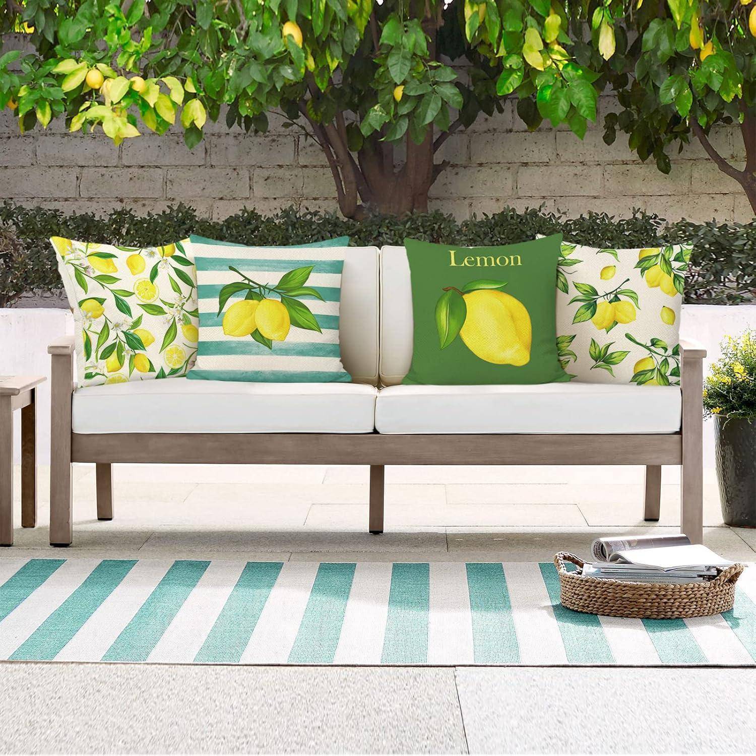 Outdoor-Terrasse mit einer weißen Bank, Zitronen-Motiv-Kissen und einem grün gestreiften Teppich. Üppiges Grün im Hintergrund verstärkt die erfrischende Atmosphäre.