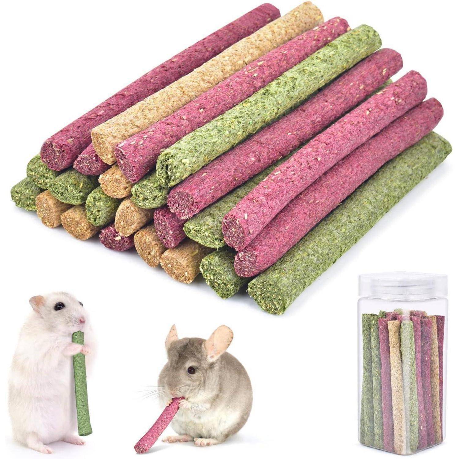 Stapel von bunten Kauholzstangen in Rosa, Grün und Beige. Ein Hamster und ein Chinchilla halten jeweils ein Stück. Ein Behälter enthält weitere Stangen.