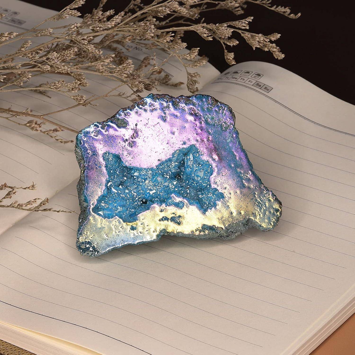 Ein bunter, schillernder Geode liegt geöffnet auf einem liniierten Notizbuch, wobei getrocknetes Laub teilweise über die Seite verteilt ist.