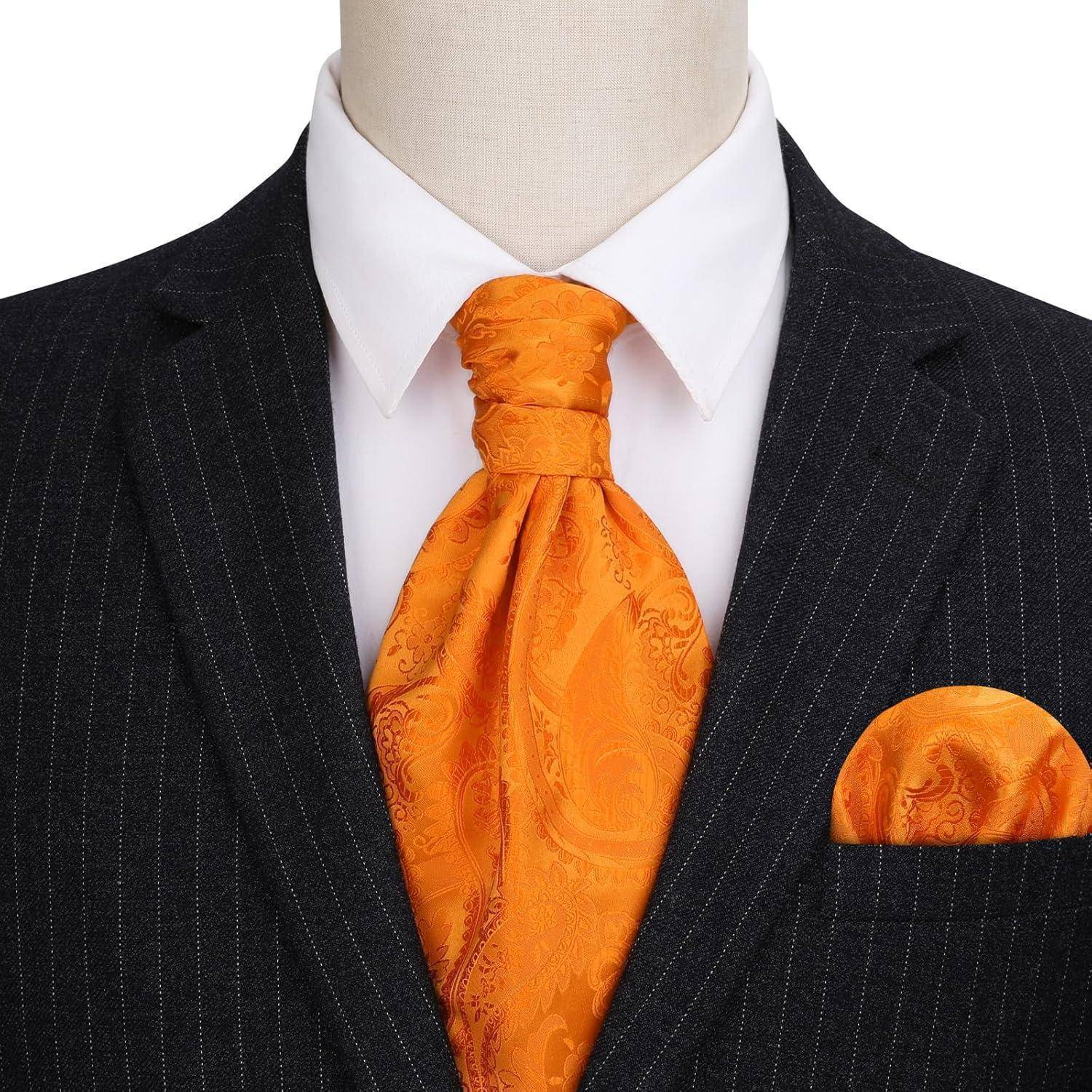 Eine Person, die einen dunklen Nadelstreifenanzug mit einer orangefarbenen Paisley-Krawatte und einem passenden Einstecktuch vor einem weißen Hintergrund trägt.
