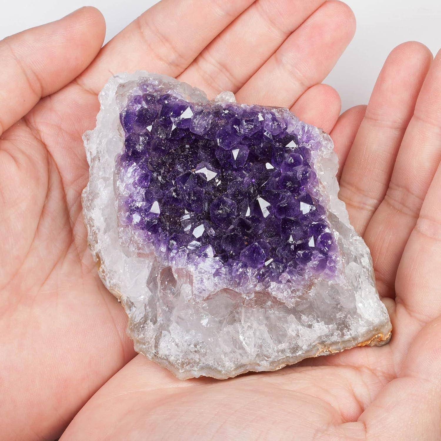 Hände, die einen violetten Amethystkristall mit rauer Außenkante halten und dessen gezackte, glitzernde Oberfläche präsentieren.