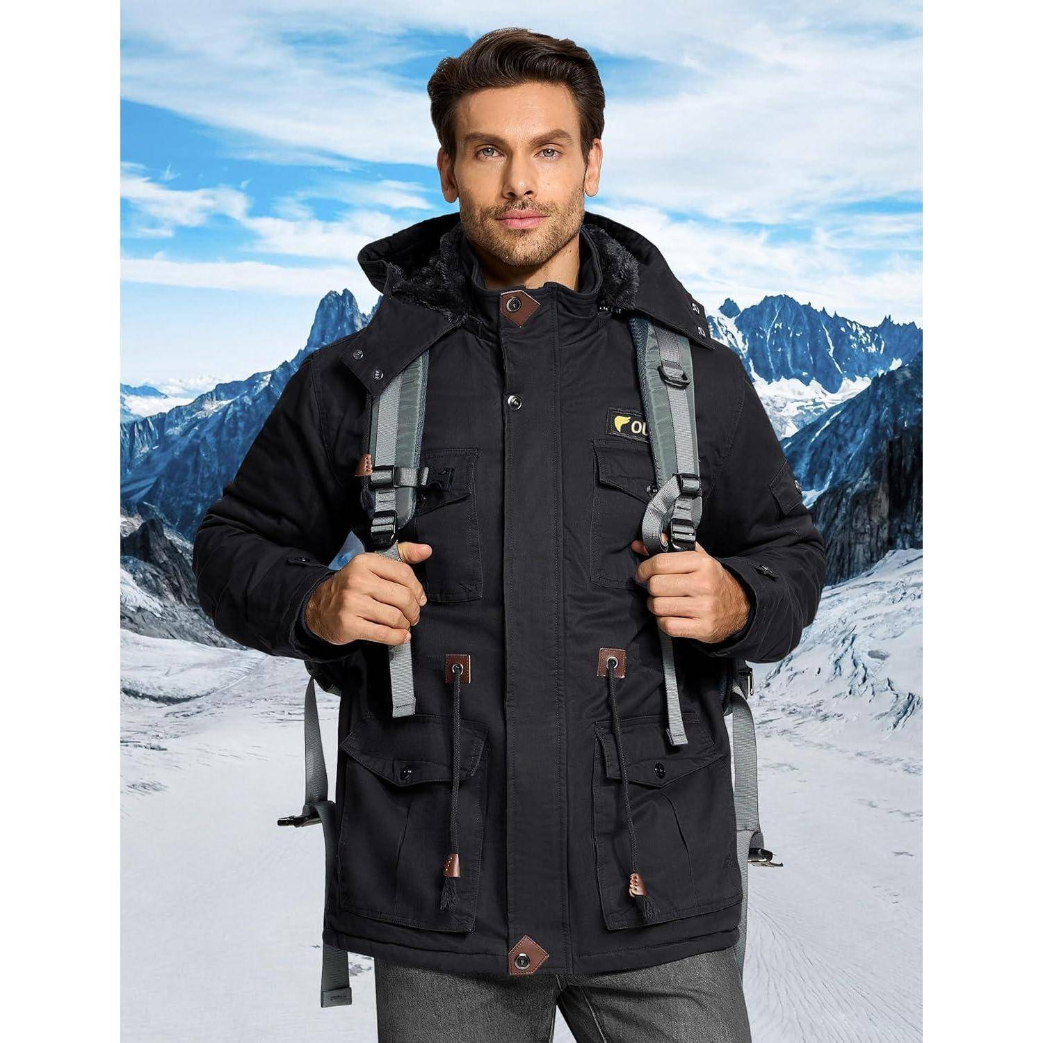 Eine Person mit einer schwarzen Winterjacke mit Kapuze und einem Rucksack steht in einer verschneiten Berglandschaft mit rauen Gipfeln im Hintergrund.