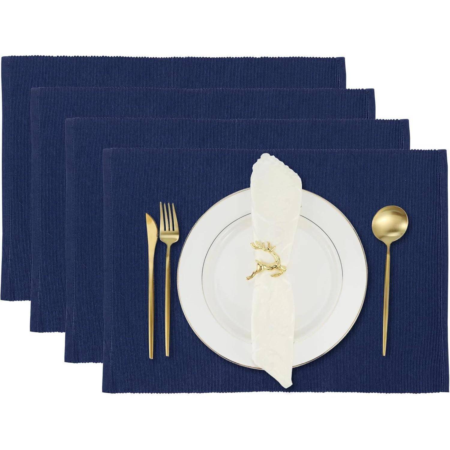Ein Gedeckter Tisch mit einem weißen Teller, einer goldenen Gabel, einem Messer und einem Löffel auf einem marineblau-farbenen Platzdeckchen. Eine weiße Serviette mit einem goldenen Ring ist auf dem Teller platziert.