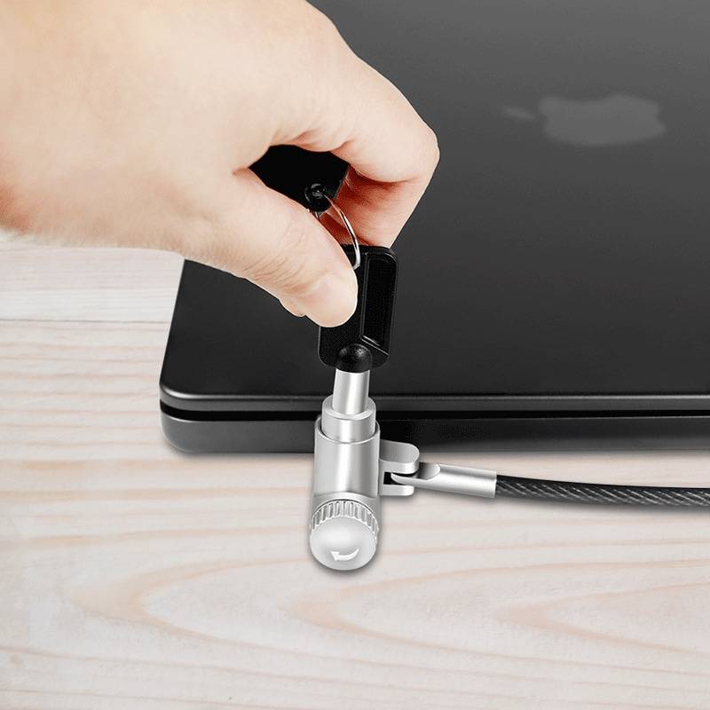 Eine Person führt ein Sicherheitskabel in den Verriegelungsanschluss eines Laptops auf einem Holzschreibtisch ein und sorgt damit für physischen Schutz vor Diebstahl.