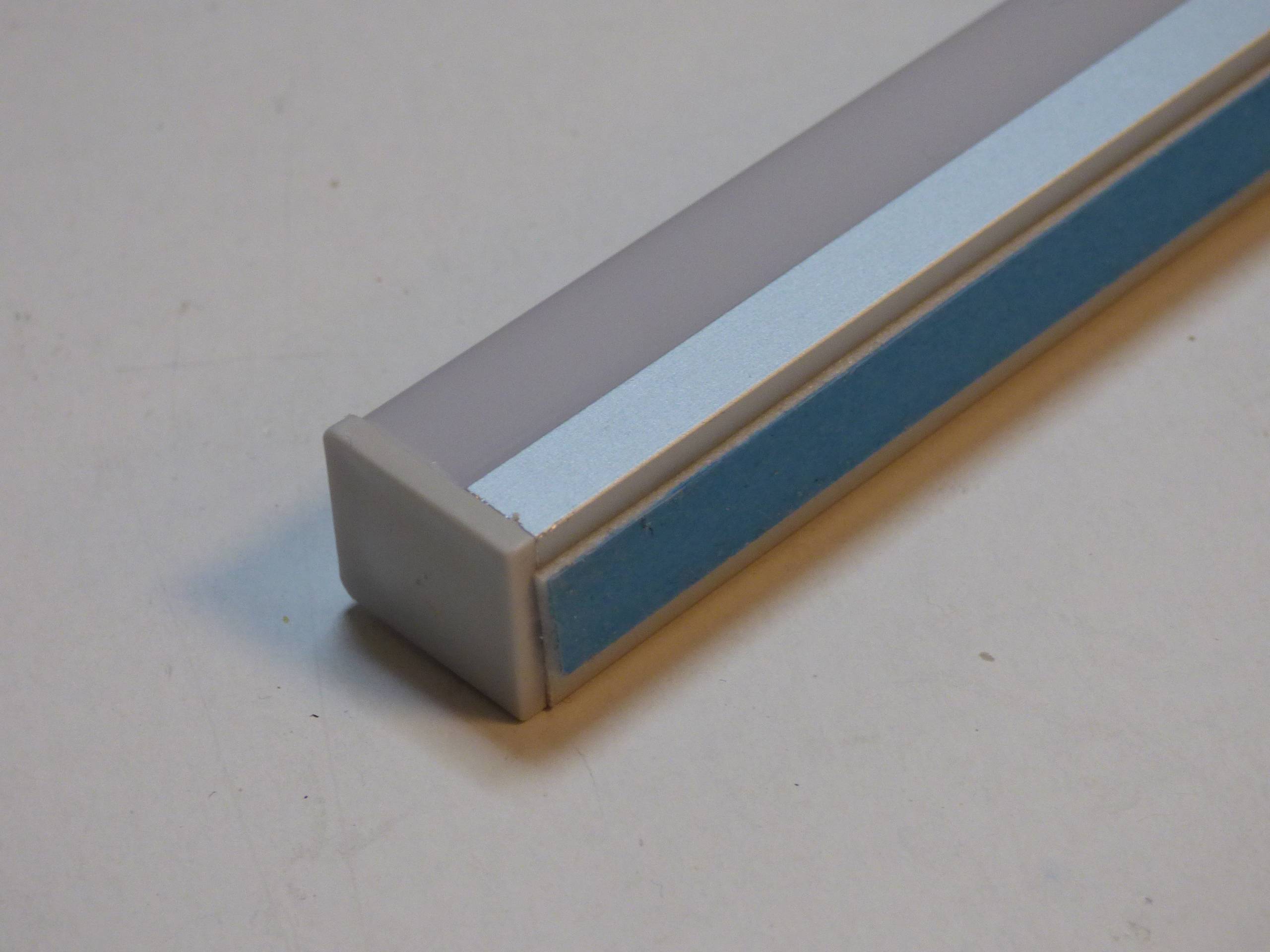 Ein rechteckiger, hellgrauer Gegenstand mit einem blauen Streifen an seiner Seite, auf einem neutralen Hintergrund platziert. Der Gegenstand scheint ein Werkzeug oder eine Stange zu sein.