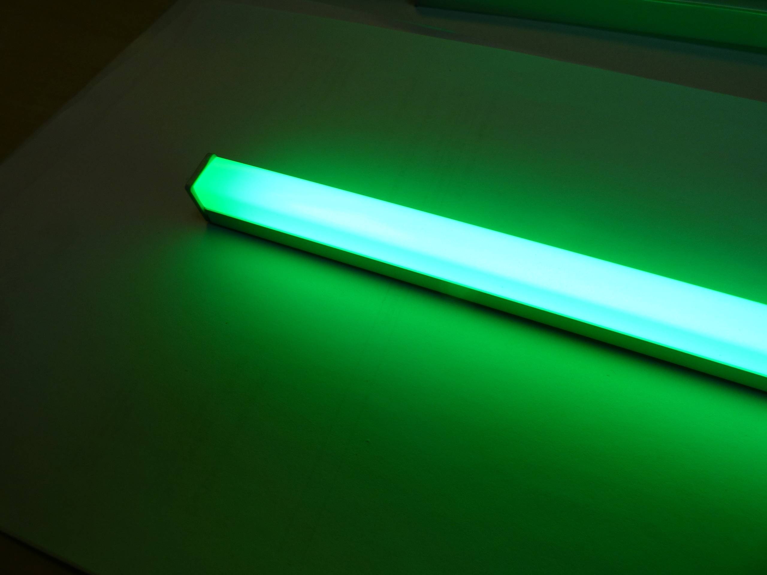 Ein leuchtender grüner Knicklichtstab, der auf einer flachen Oberfläche platziert ist und eine helle grüne Leuchtkraft um sich herum verbreitet.