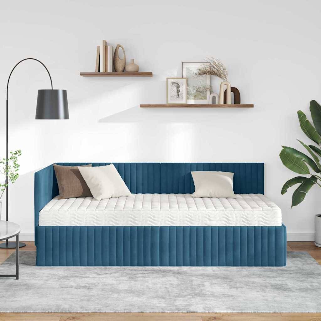Ein moderner Wohnraum zeigt ein blaues Tagesbett mit cremefarbenen Kissen, eine schwarze Stehlampe, schwebende Regale mit Dekoration und eine große Pflanze.