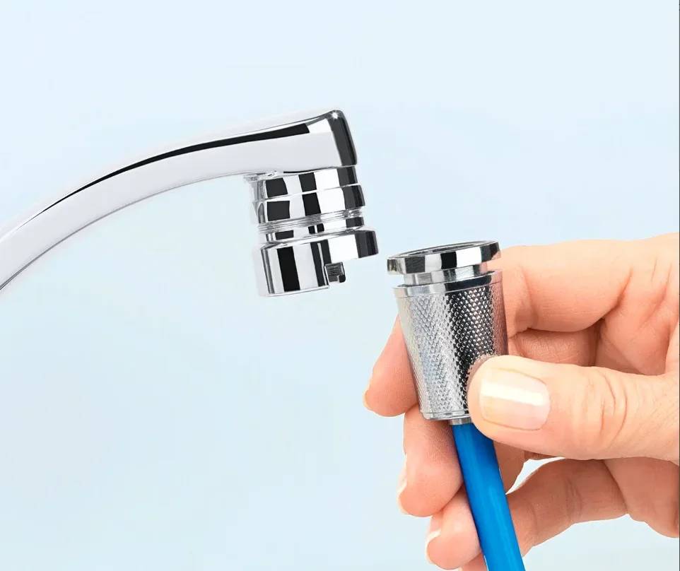 Eine Hand verwendet ein Werkzeug mit blauem Griff, um den Luftsprudler von einem Chrom-Wasserhahn für Wartungs- oder Reinigungszwecke zu entfernen.
