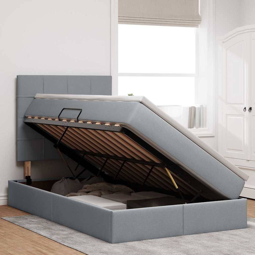 Ein modernes Schlafzimmer zeigt ein stilvolles, grau gepolstertes Ottomane-Bett mit erhöhtem Stauraum, unter einem sonnendurchfluteten Fenster und neben weißen Schränken.