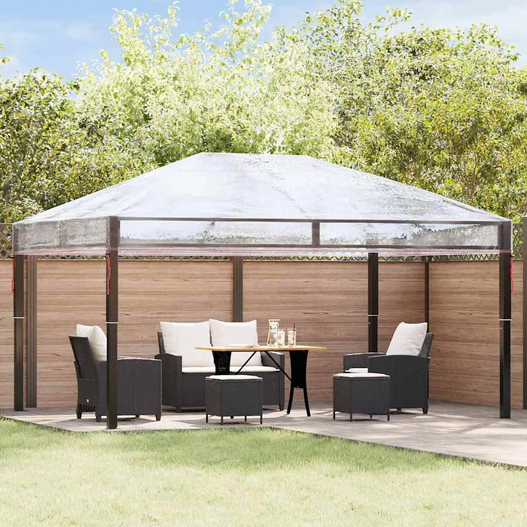 Ein Pavillon mit transparentem Dach steht auf einer Holzterrasse. Er ist mit schwarzen Korbstühlen und einem Tisch unter einem sonnigen Himmel eingerichtet.