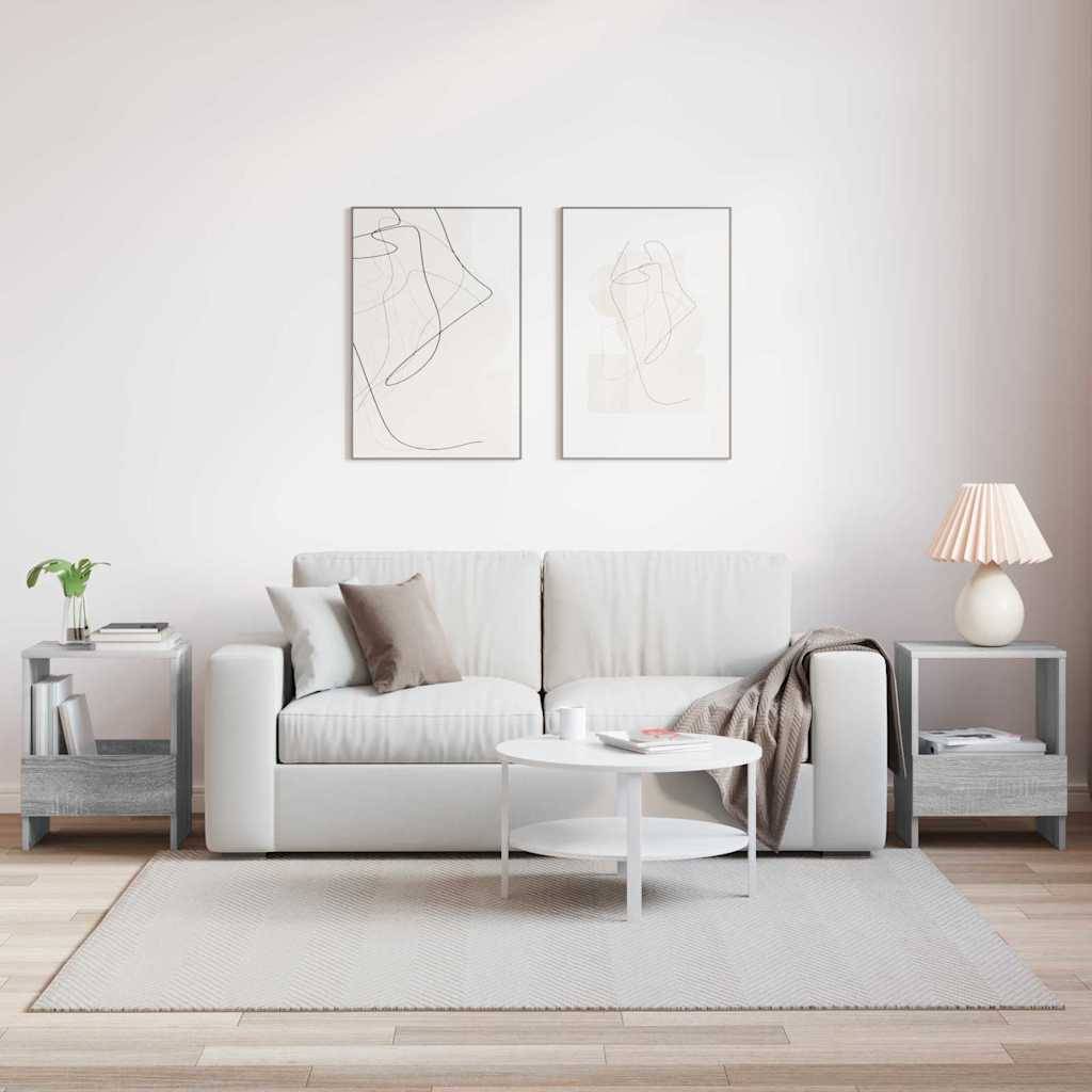 Ein moderner Wohnraum präsentiert ein weißes Sofa mit beigen Kissen, einen runden weißen Couchtisch, graue Beistelltische und abstrakte Wandkunst.