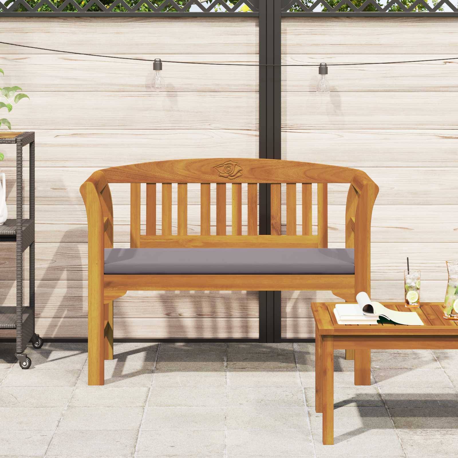 Eine Holzbank mit einem Kissen steht auf einer Terrasse neben einem kleinen Tisch mit Getränken, vor einem Zaun mit Lichterketten.