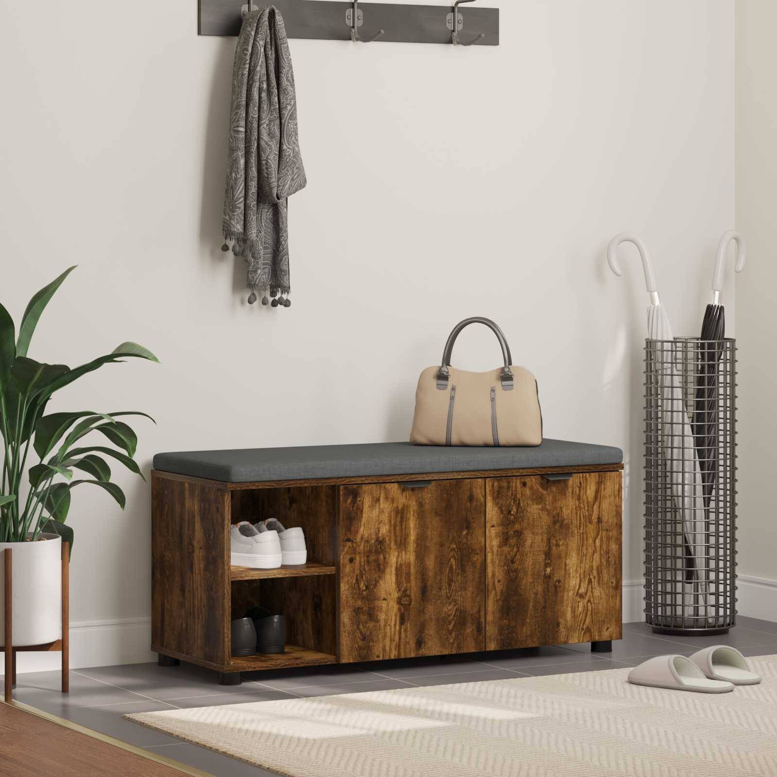 Eine Holzbank mit Stauraum befindet sich in einem modernen Eingangsbereich und enthält Schuhe und eine Tasche. Mäntel hängen darüber. Eine Pflanze und ein Regenschirmständer sind in der Nähe.