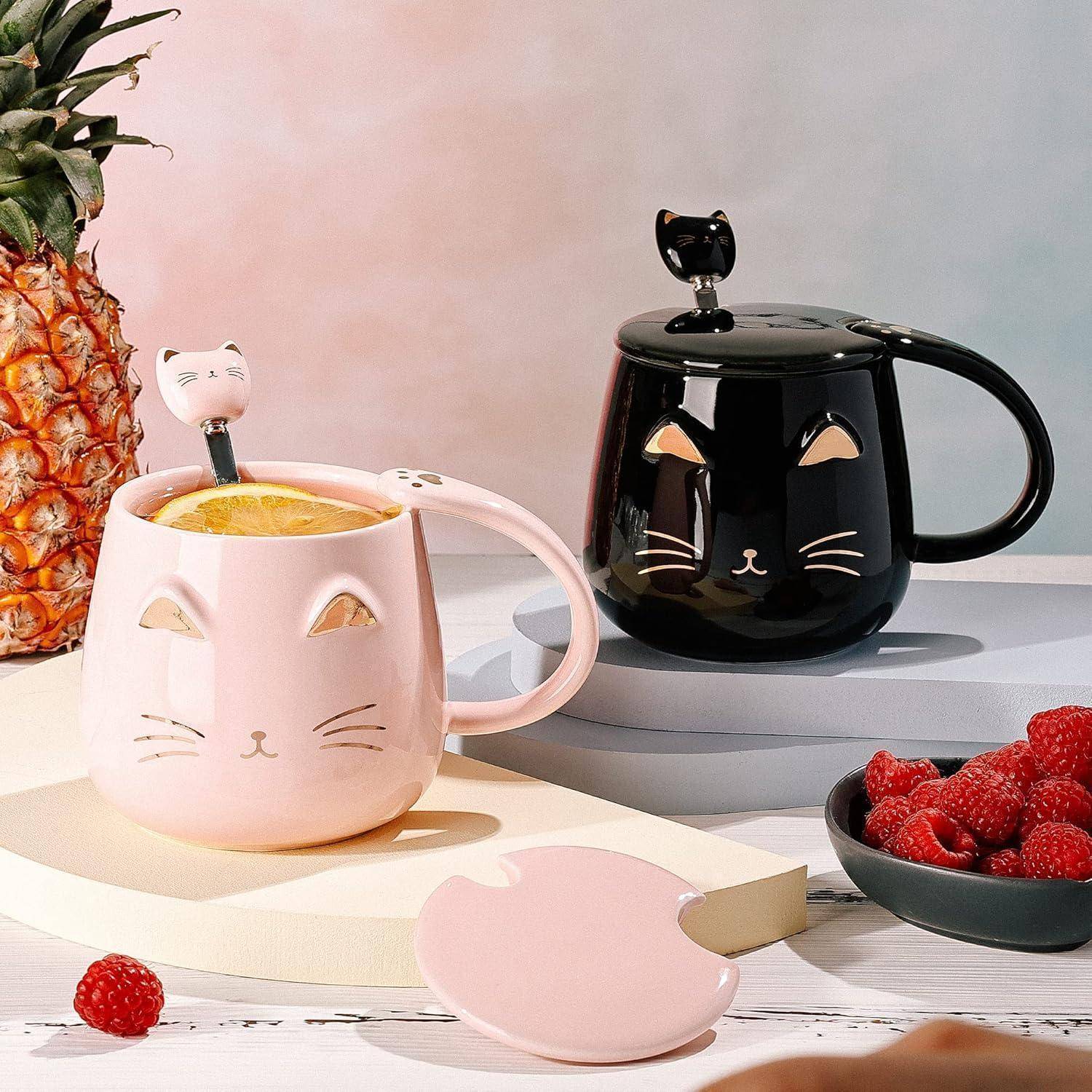 Zwei Katzen-Tassen, eine in Pink, die andere in Schwarz, mit Deckeln und Zitronenscheiben im Inneren. Eine Ananas und eine Schüssel mit Himbeeren befinden sich in der Nähe.